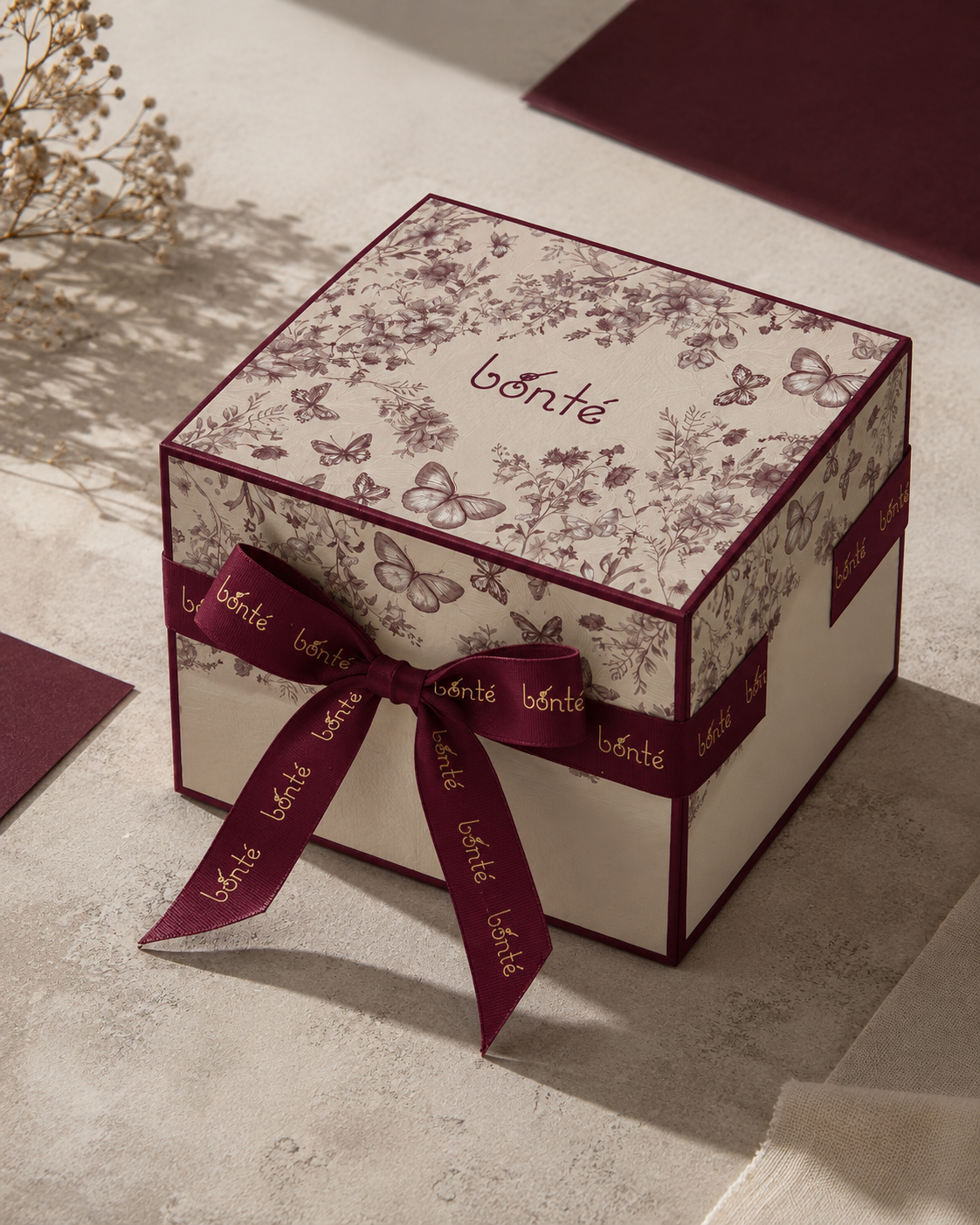 Caja de regalo Bonté cerrada con lazo burdeos y patrón floral en la tapa.