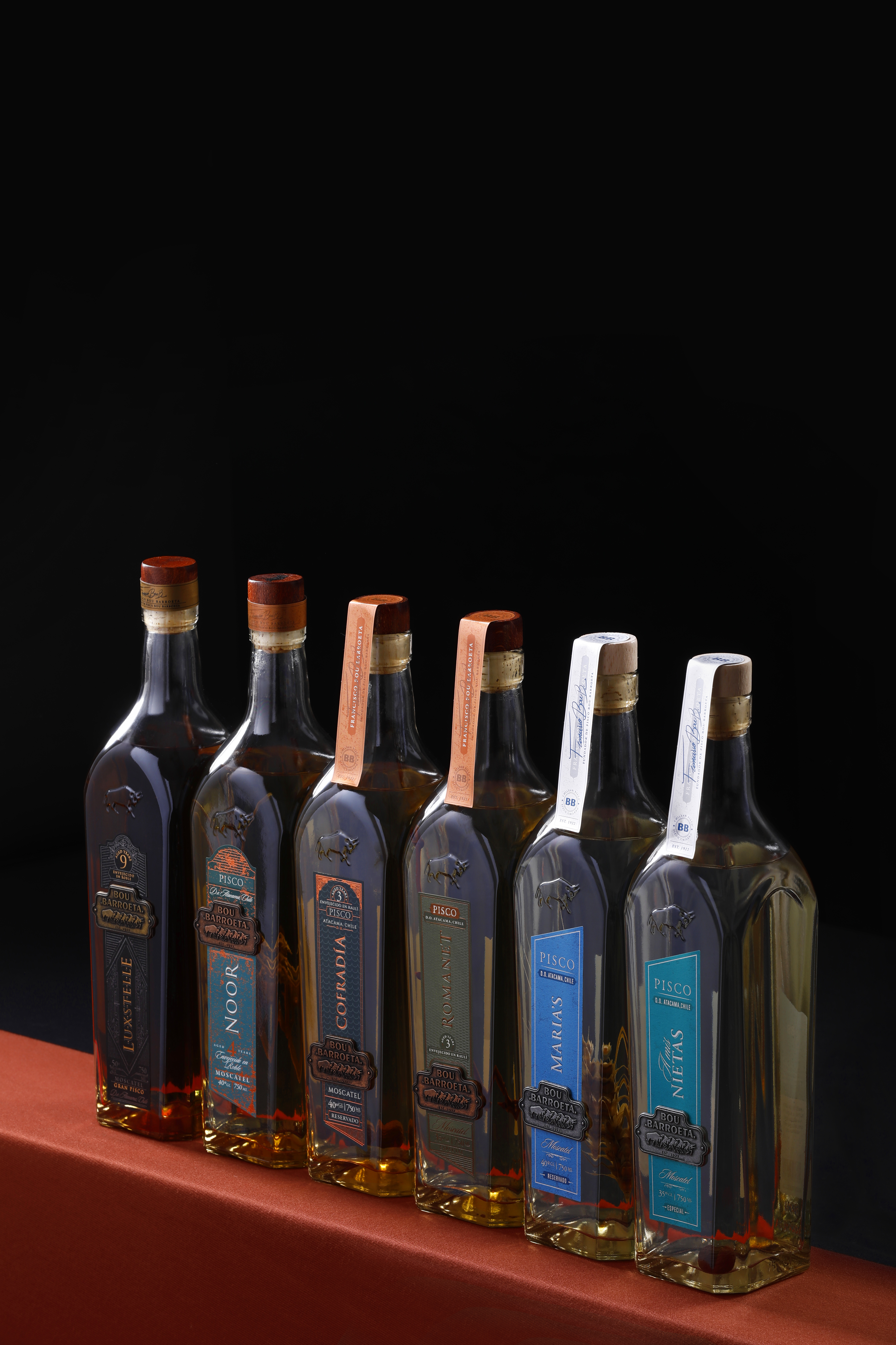 Familia de botellas Bou Barroeta alineadas sobre una base roja y un fondo oscuro.