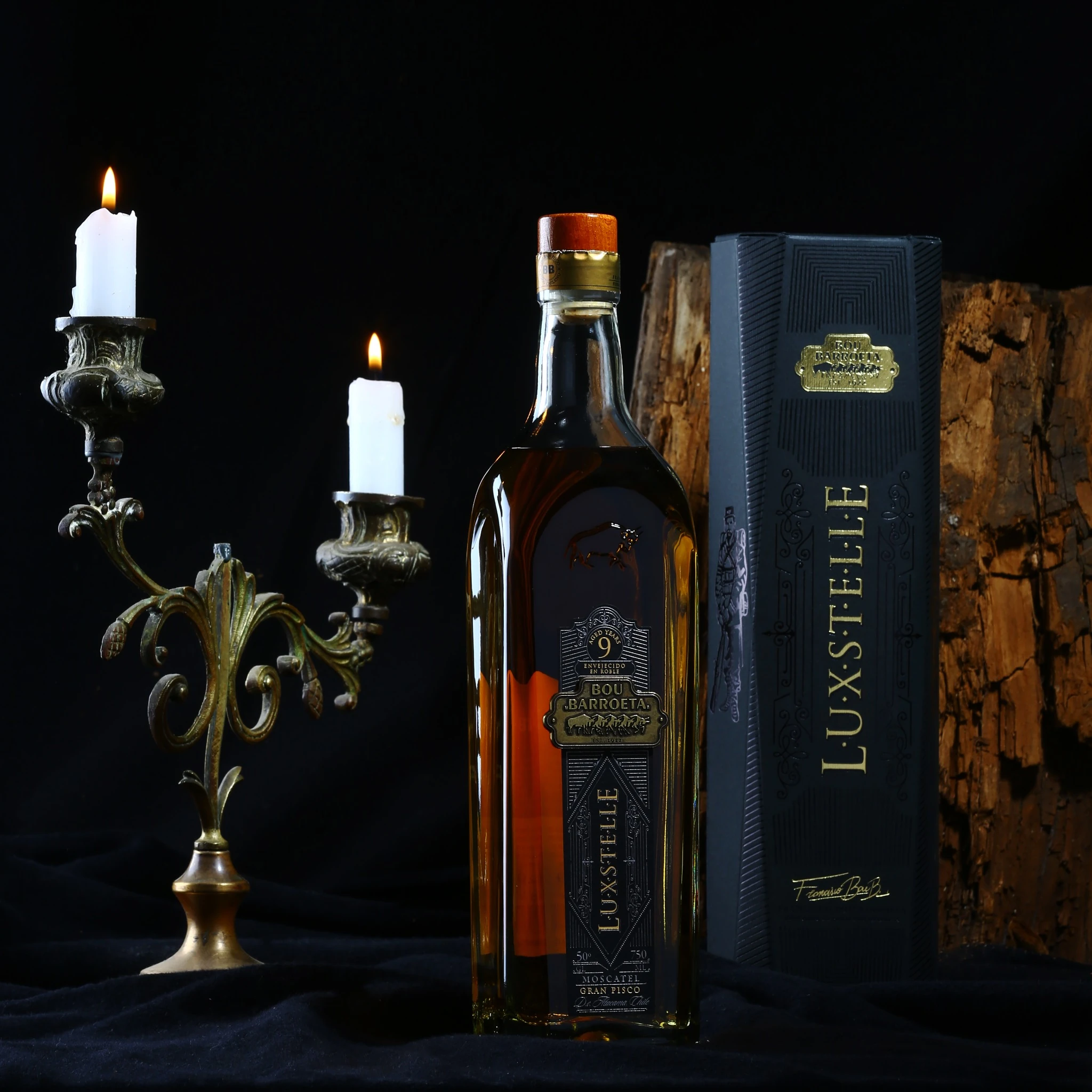 Botella Luxstelle de Bou Barroeta junto a su estuche negro, entre candelabros y un tronco de madera.