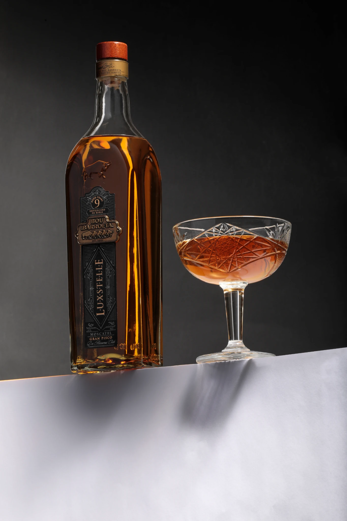 Botella Luxstelle de Bou Barroeta junto a una copa coupe servida, sobre fondo oscuro.