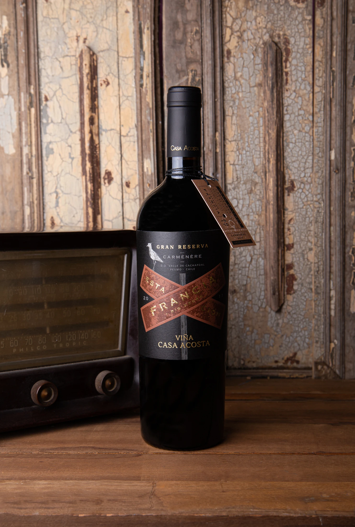 Botella Estación Francia Gran Reserva Carménère junto a una radio antigua, sobre madera descascarada.