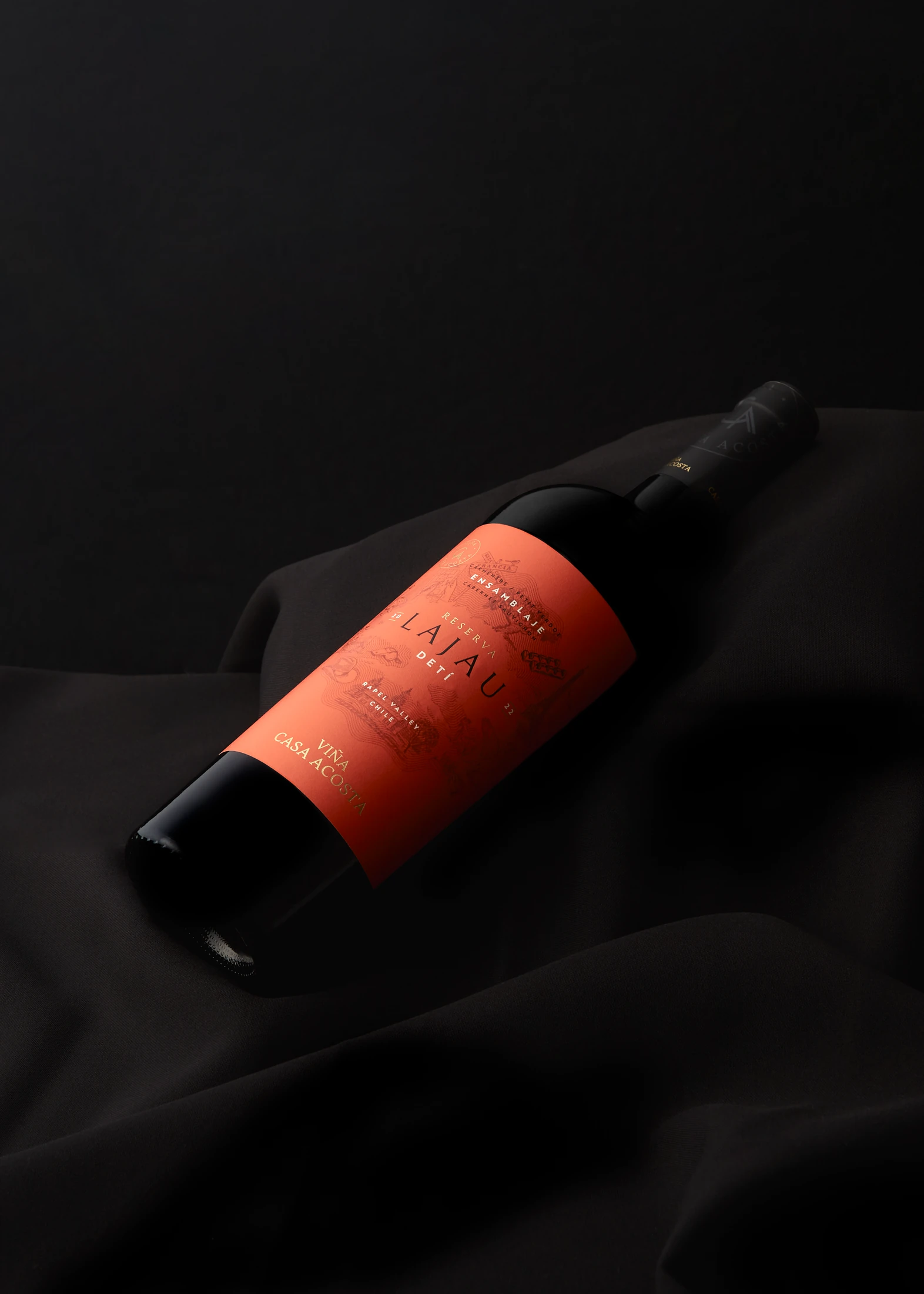 Botella Lajau DETÍ con la etiqueta naranja sobre seda negra, iluminada contra un fondo en penumbra.