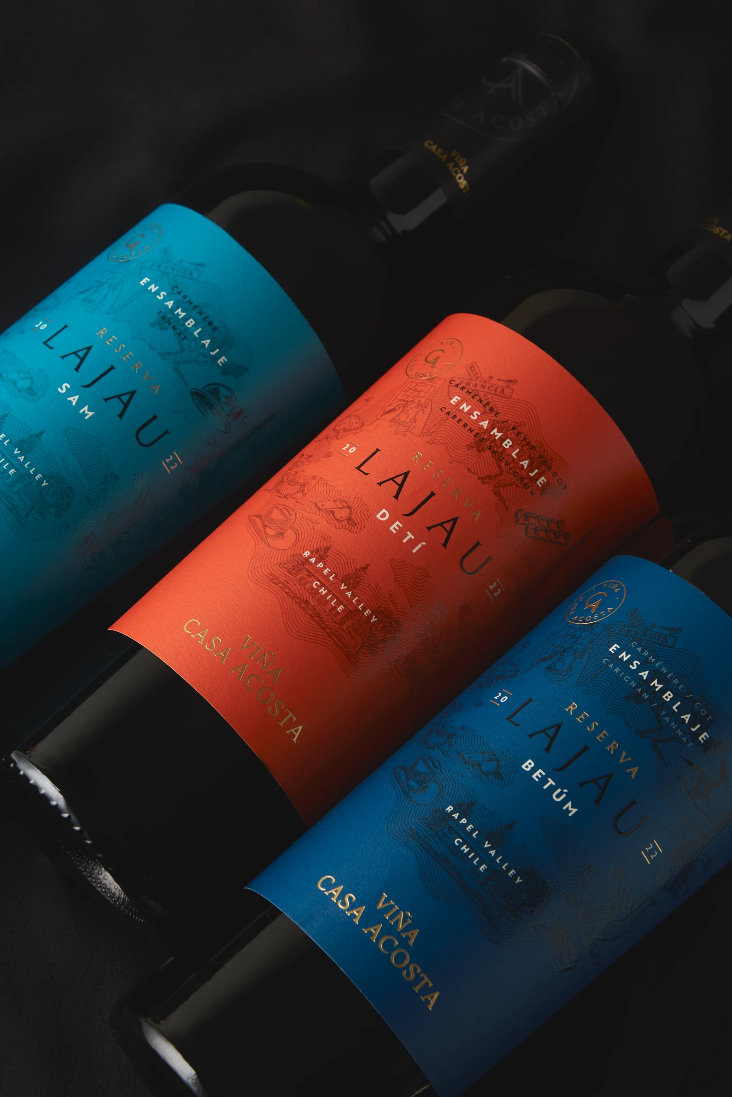 Tres botellas Lajau —SAM, DETÍ y BETÚM— con etiquetas celeste, naranja y azul sobre seda negra.