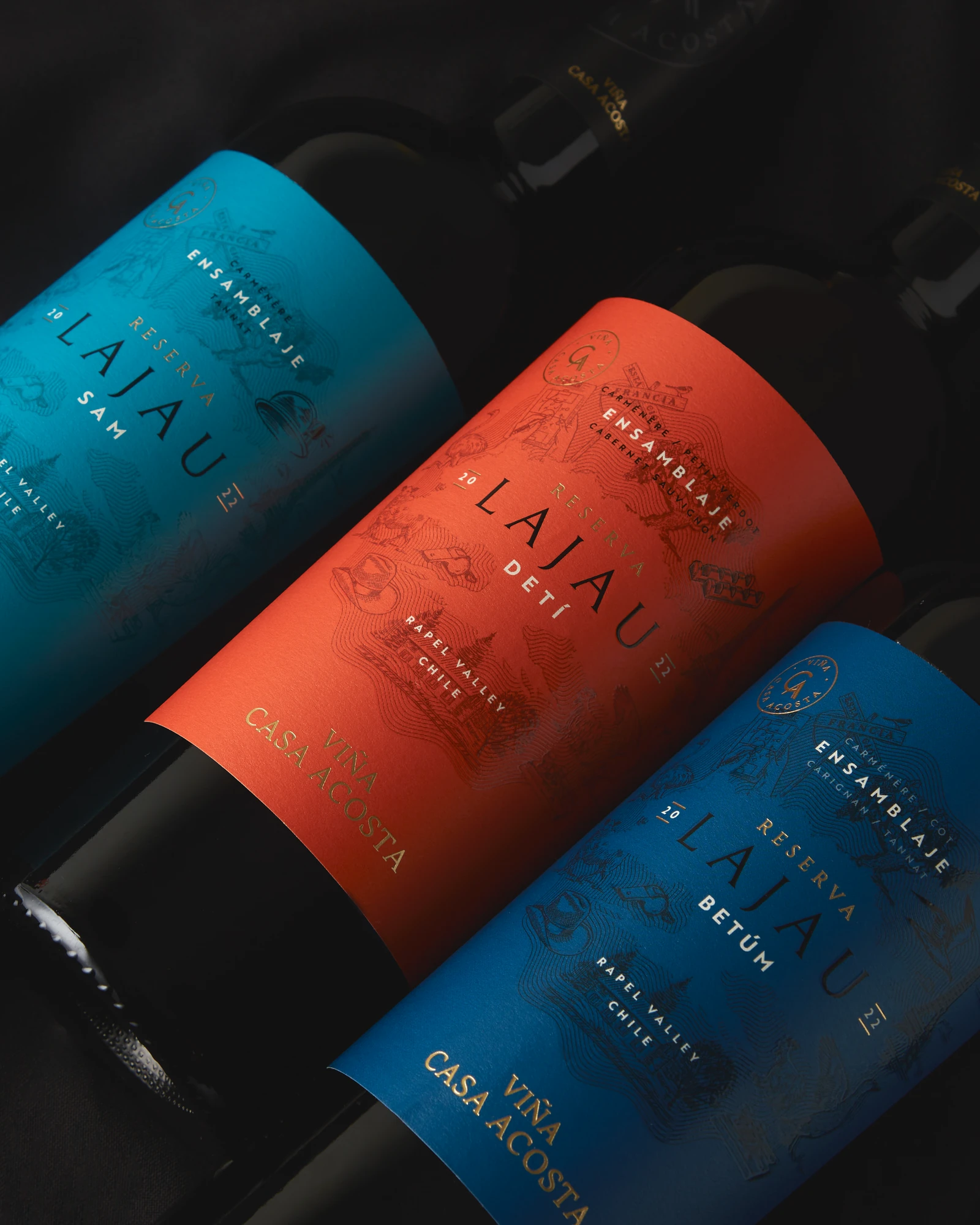 Tres botellas Lajau con etiquetas celeste, naranja y azul sobre seda negra.
