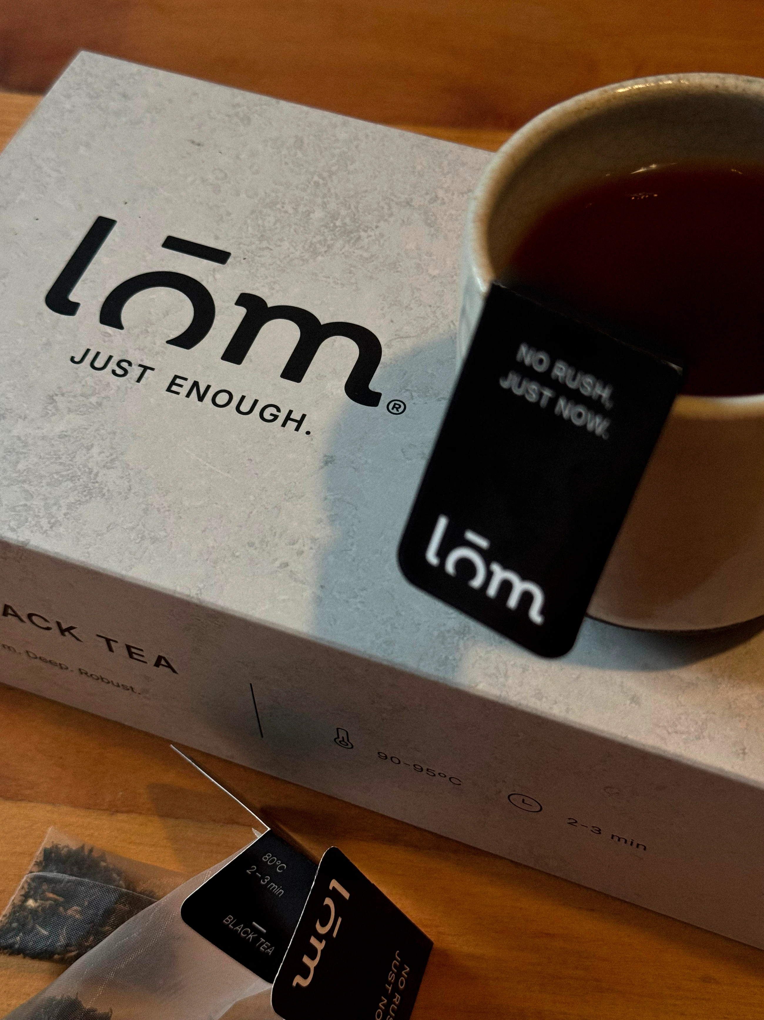 Caja LŌM, taza de té y etiqueta de anclaje sobre una mesa de madera.
