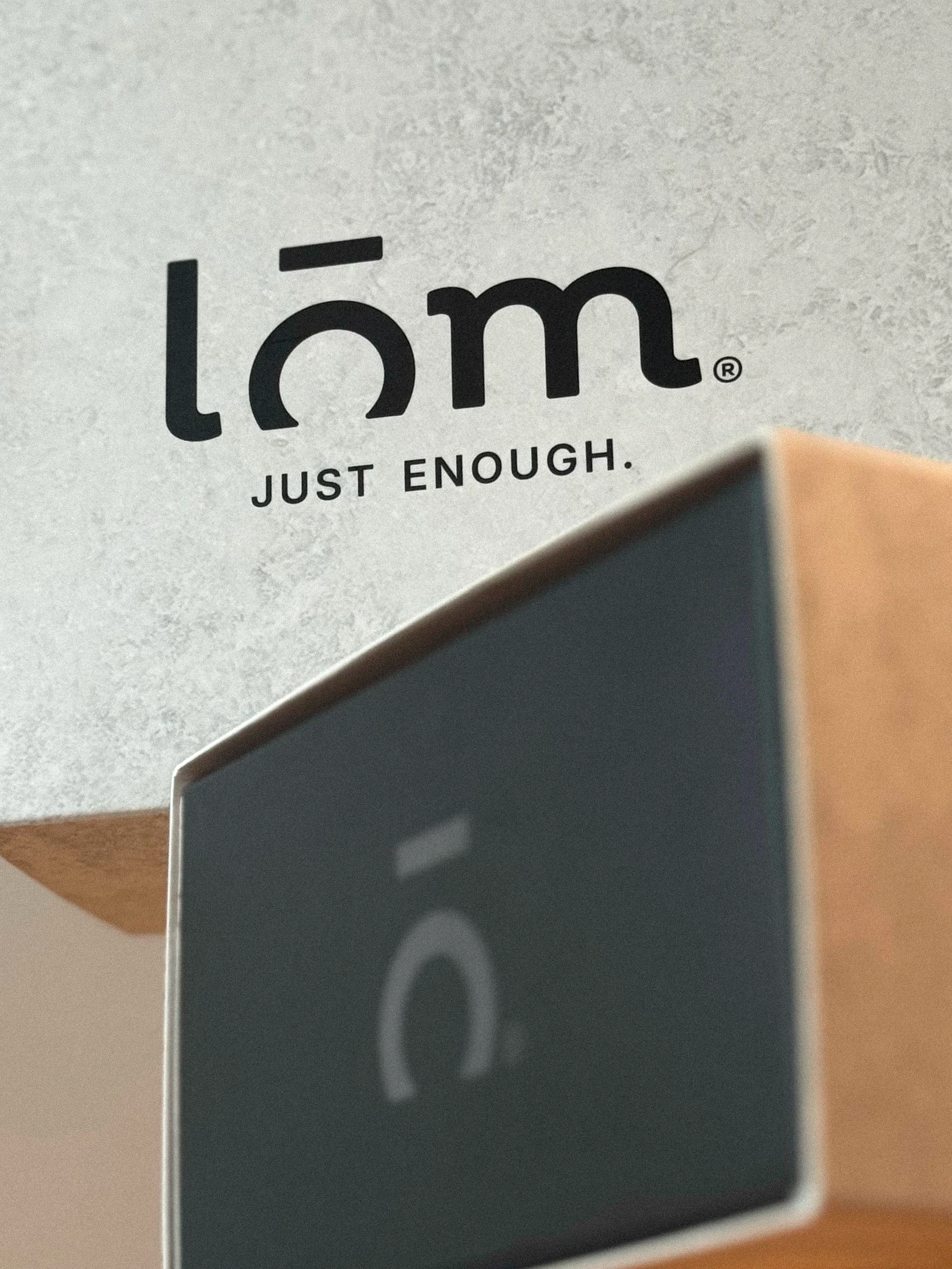 Detalle del logotipo LŌM sobre una caja clara y del isotipo sobre una caja negra.