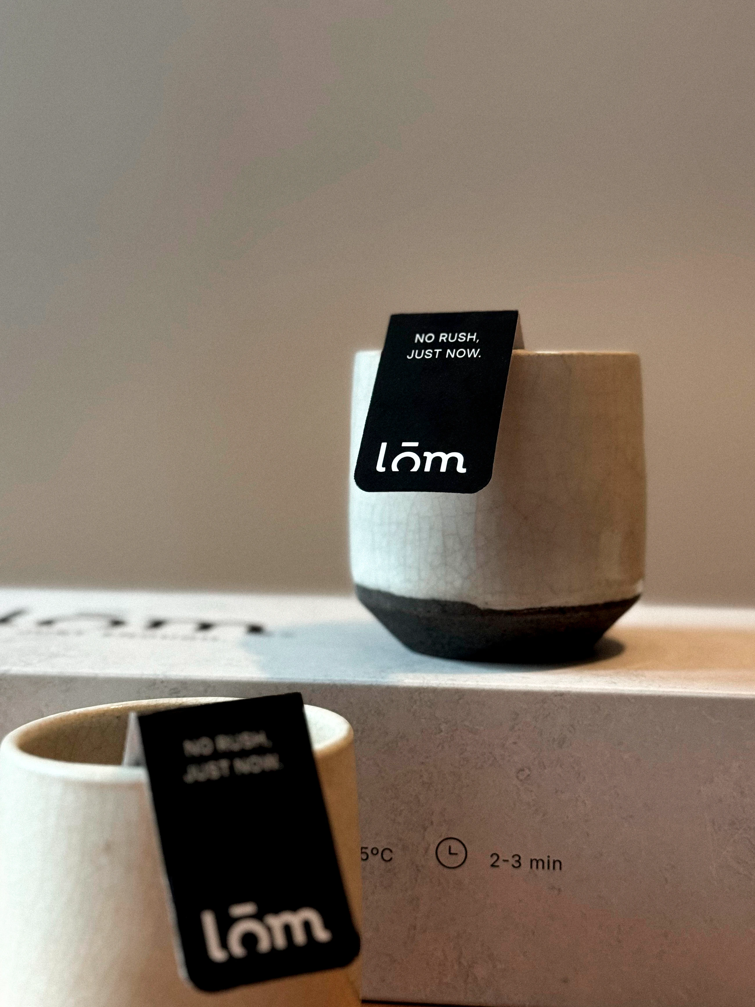Dos tazas con etiquetas LŌM ancladas al borde durante la preparación del té.