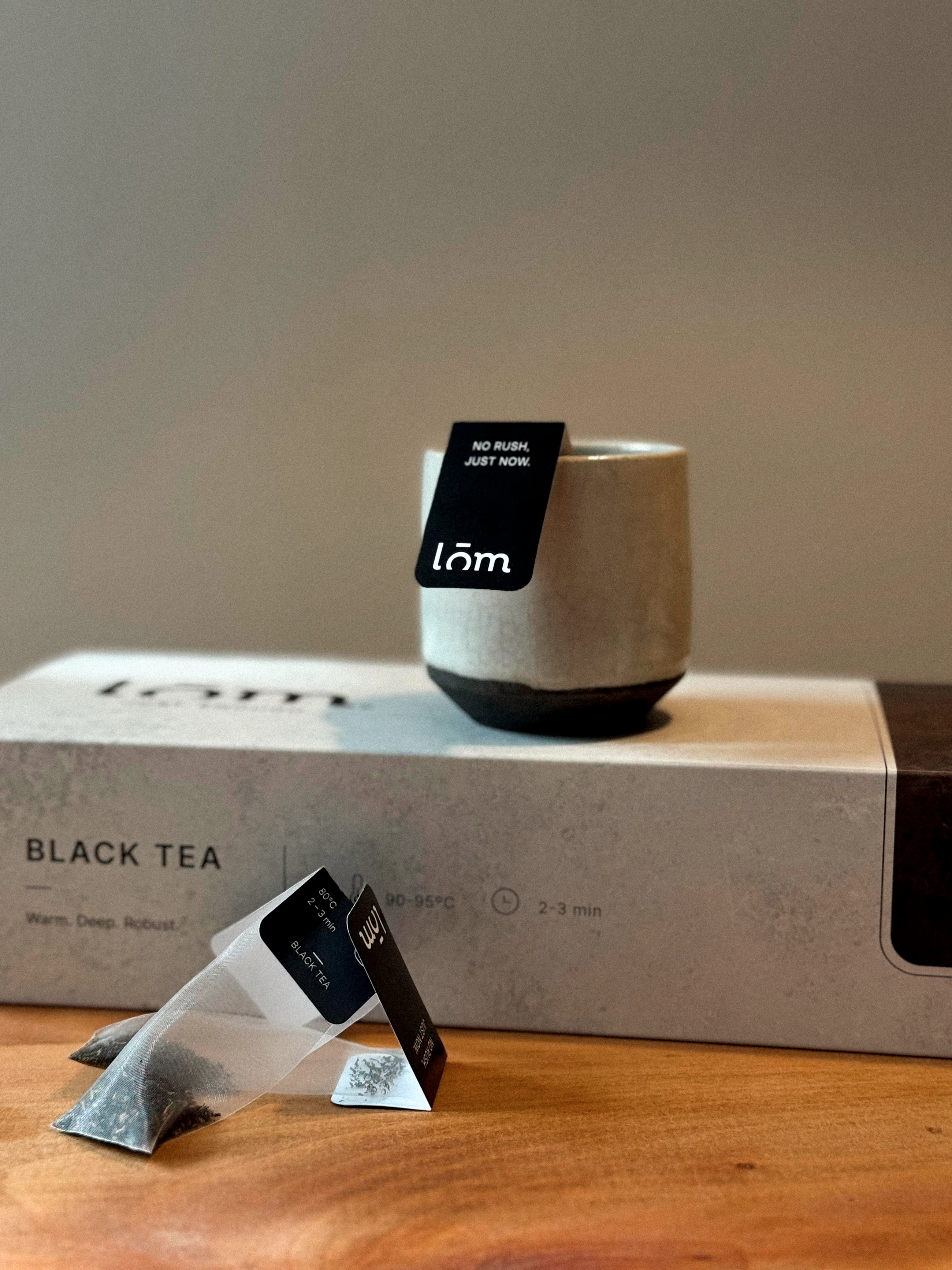 Caja de té negro LŌM, taza y unidades individuales desplegadas sobre una mesa.