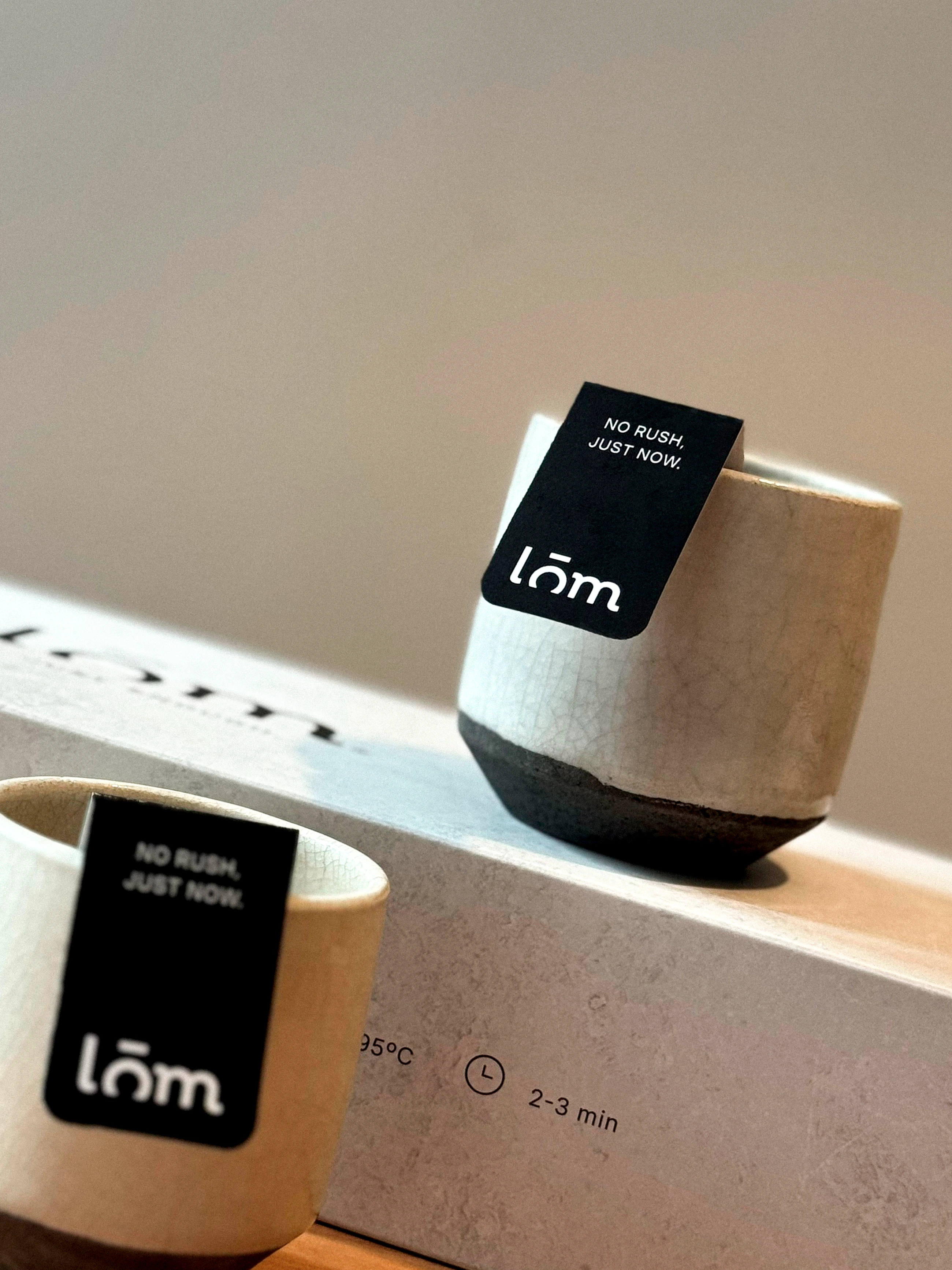 Dos tazas con etiquetas LŌM y una caja de té negro al fondo.