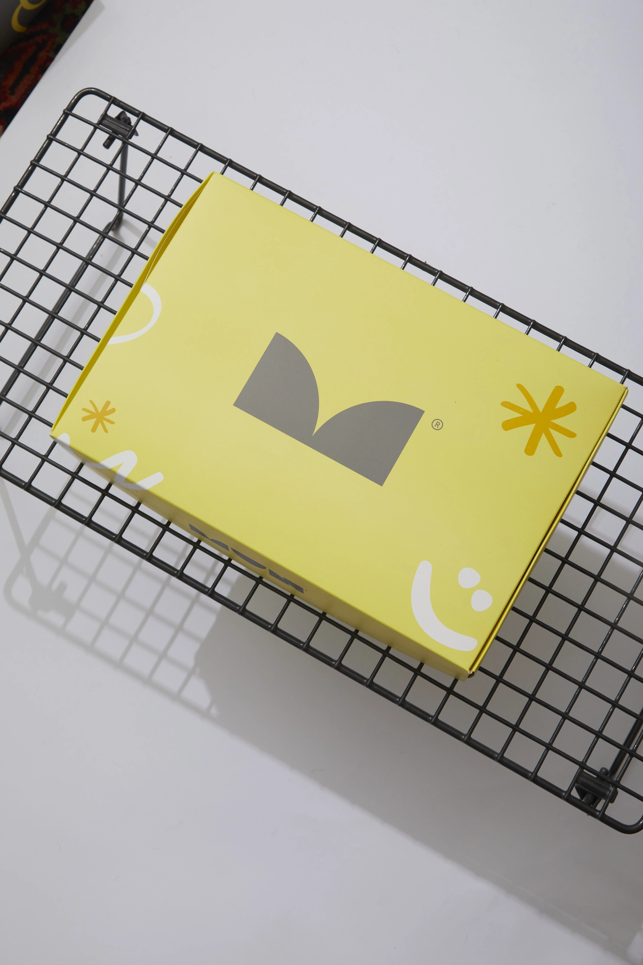 Caja rectangular amarilla de MUN con isotipo gris y elementos gráficos blancos y mostaza.
