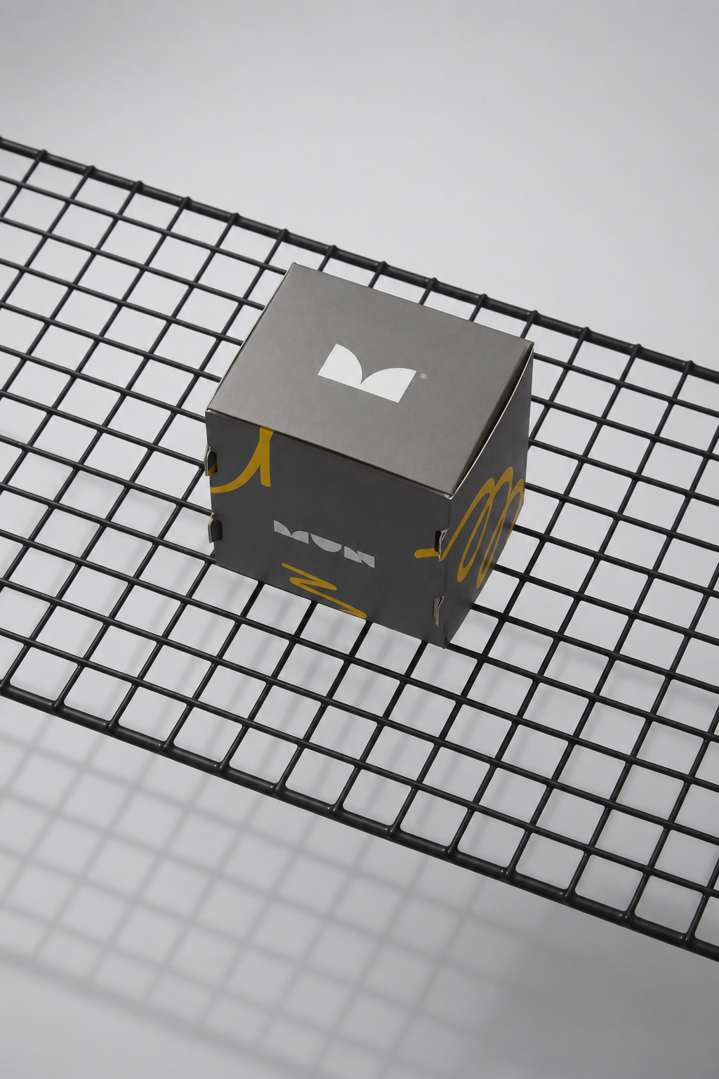 Caja cúbica gris de MUN con isotipo blanco y detalles amarillos.