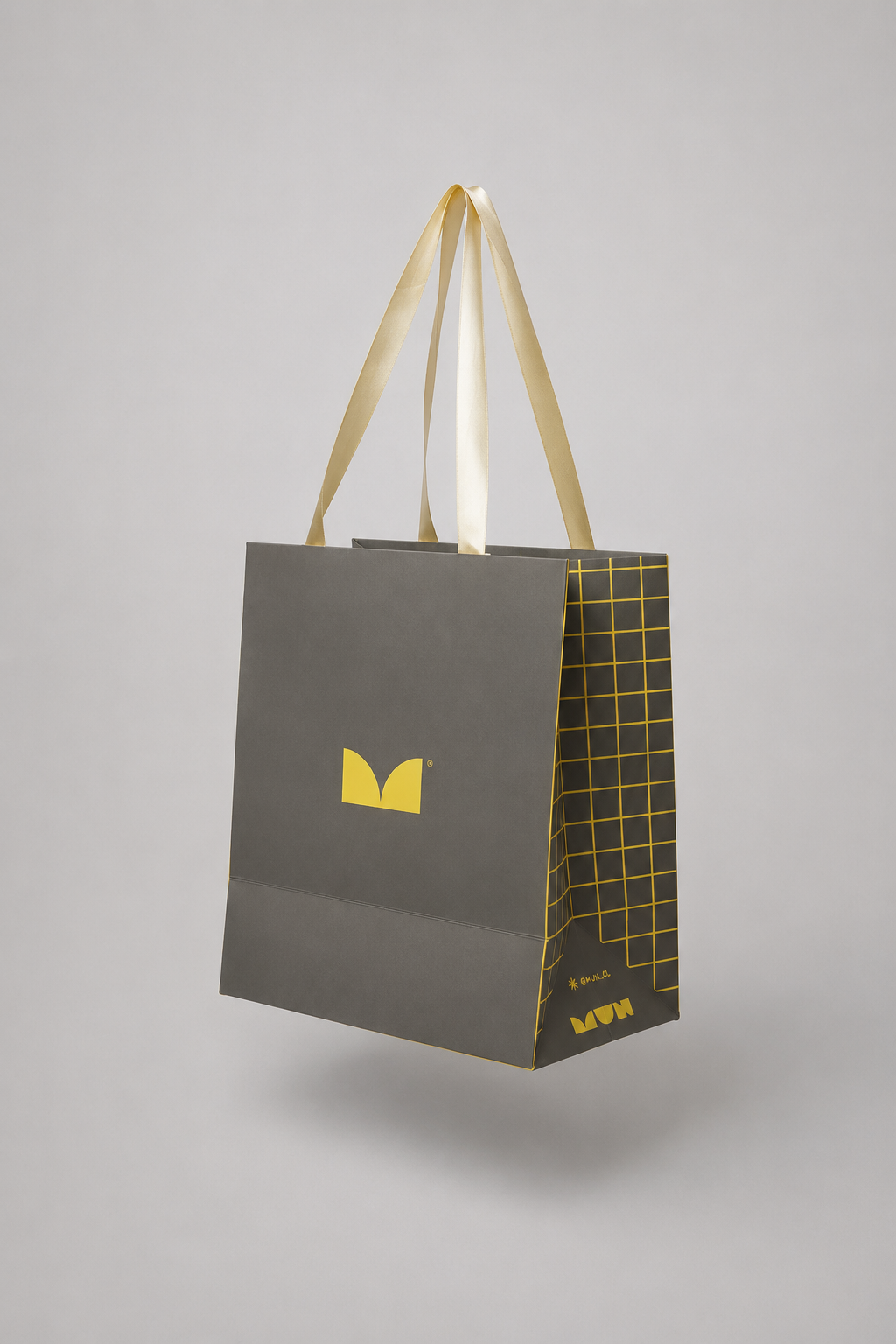 Bolsa MUN gris con asas claras, isotipo amarillo y retícula lateral.