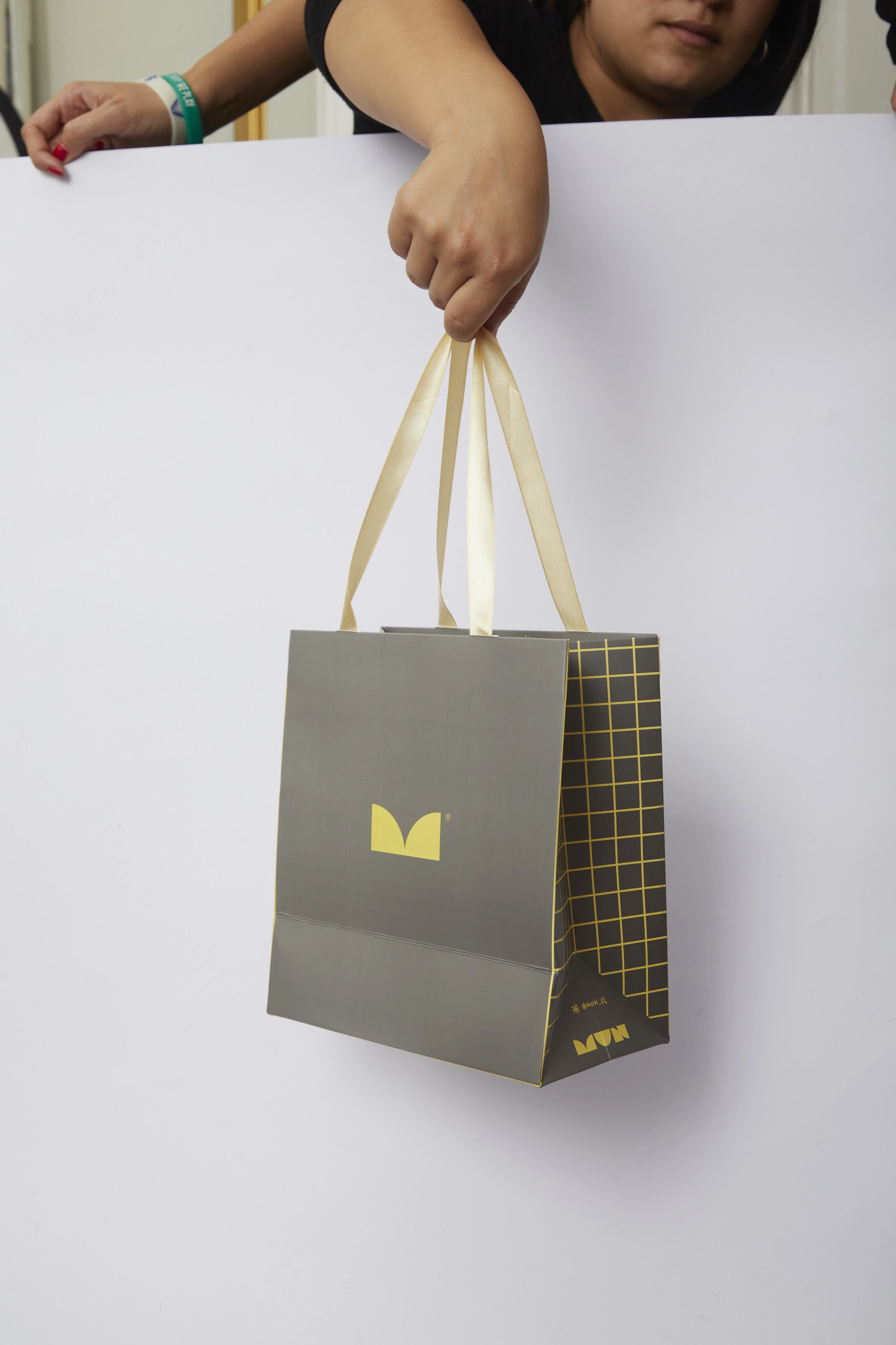 Bolsa MUN gris con asas claras, isotipo amarillo y retícula lateral.