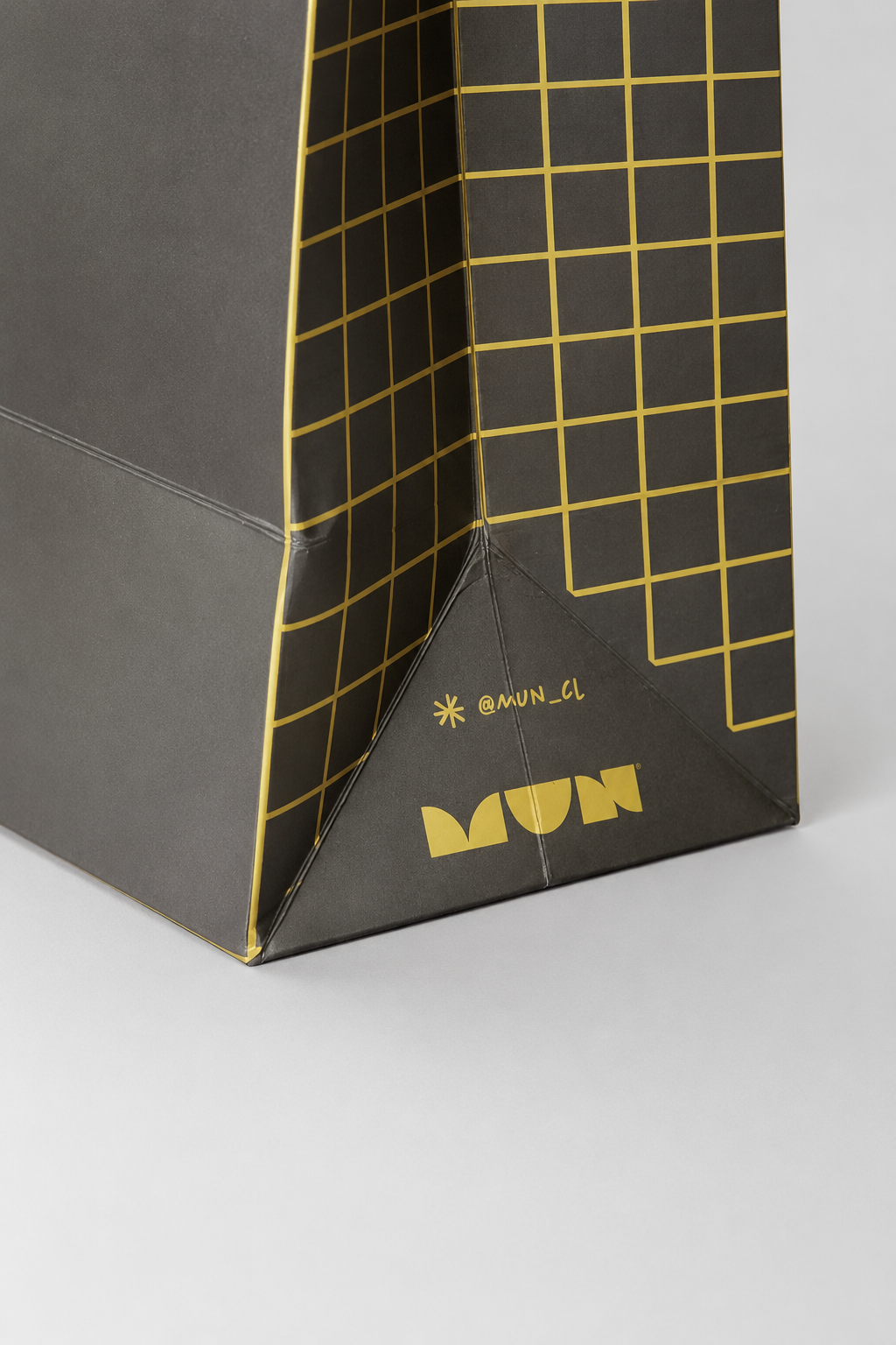 Detalle lateral de una bolsa MUN con retícula amarilla, logotipo y usuario @mun_cl.
