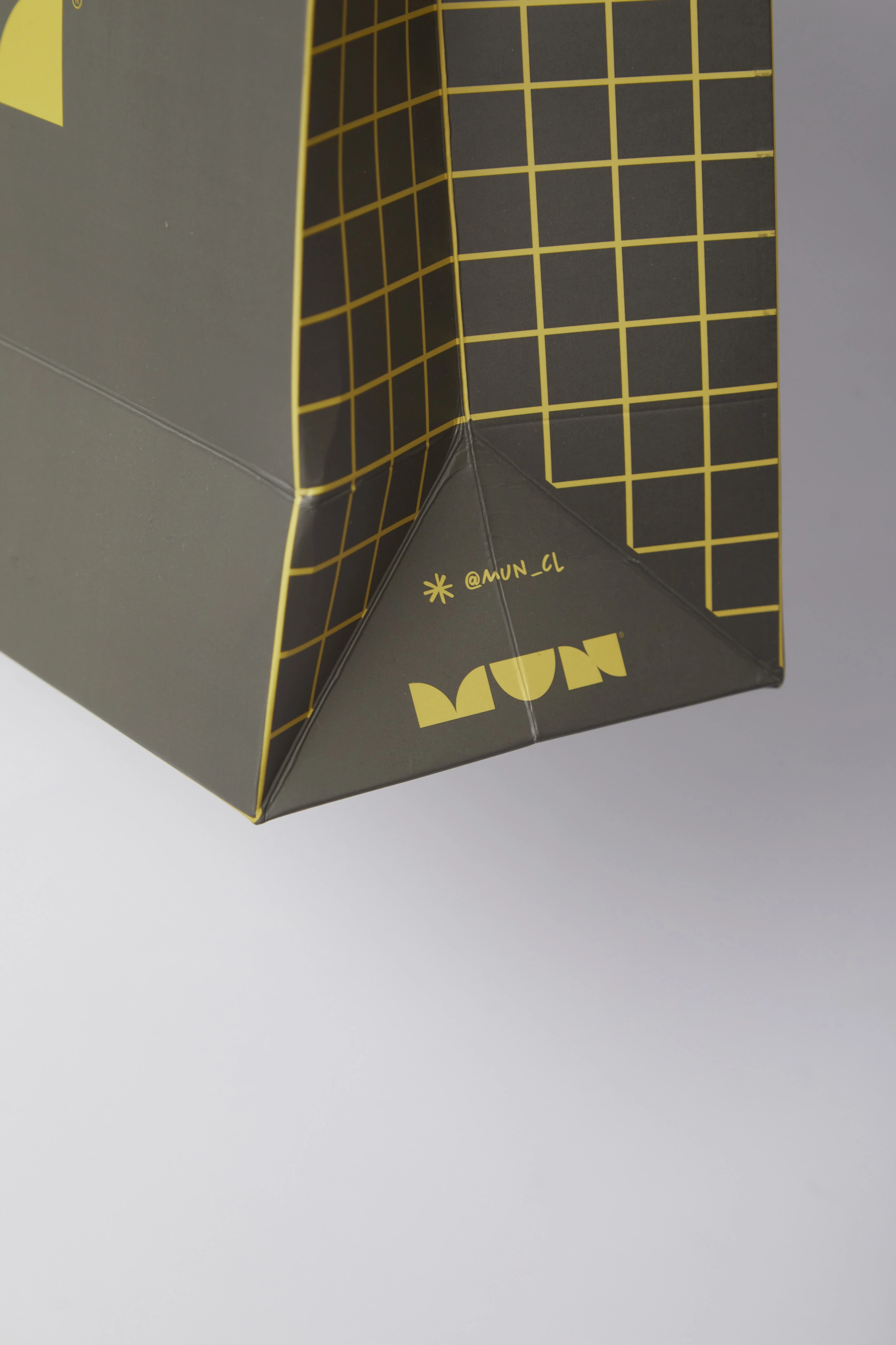 Detalle lateral de una bolsa MUN con retícula amarilla, logotipo y usuario @mun_cl.