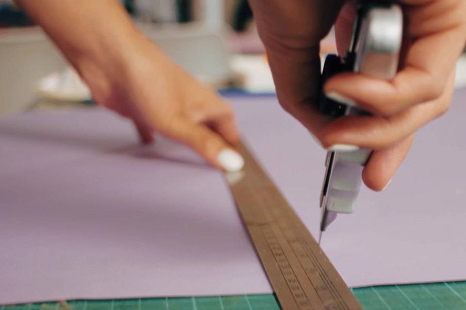 Manos midiendo y cortando papel con regla metálica sobre la mesa de trabajo