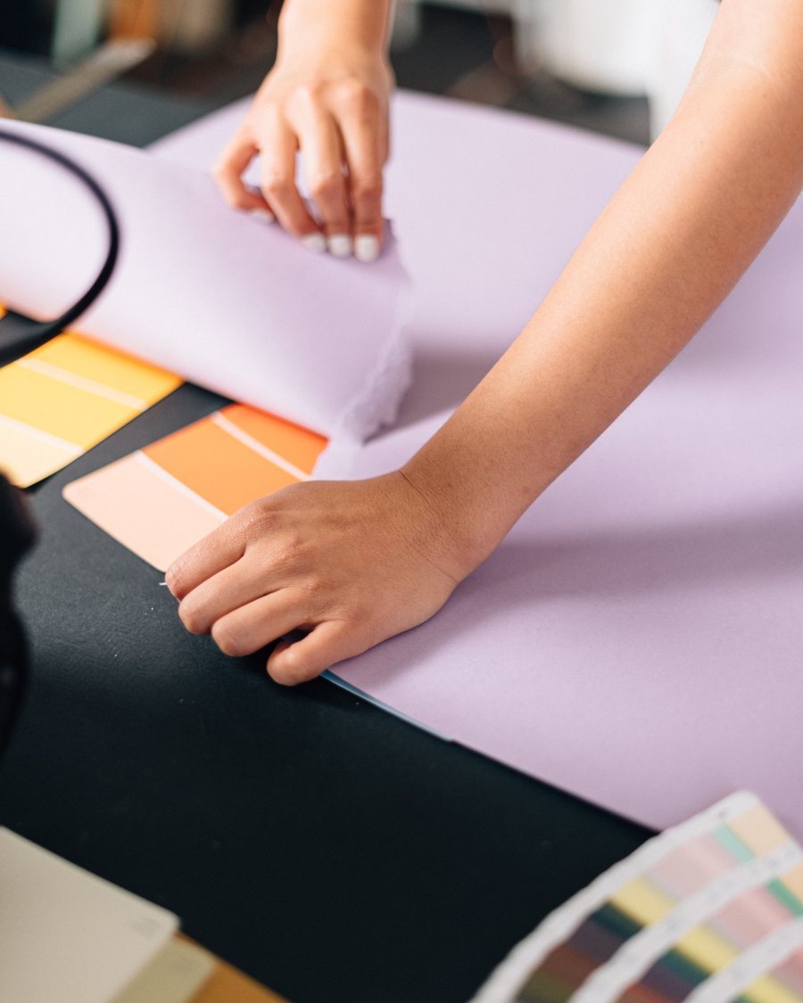 Manos alisando papel lila junto a abanicos de color sobre mesa negra