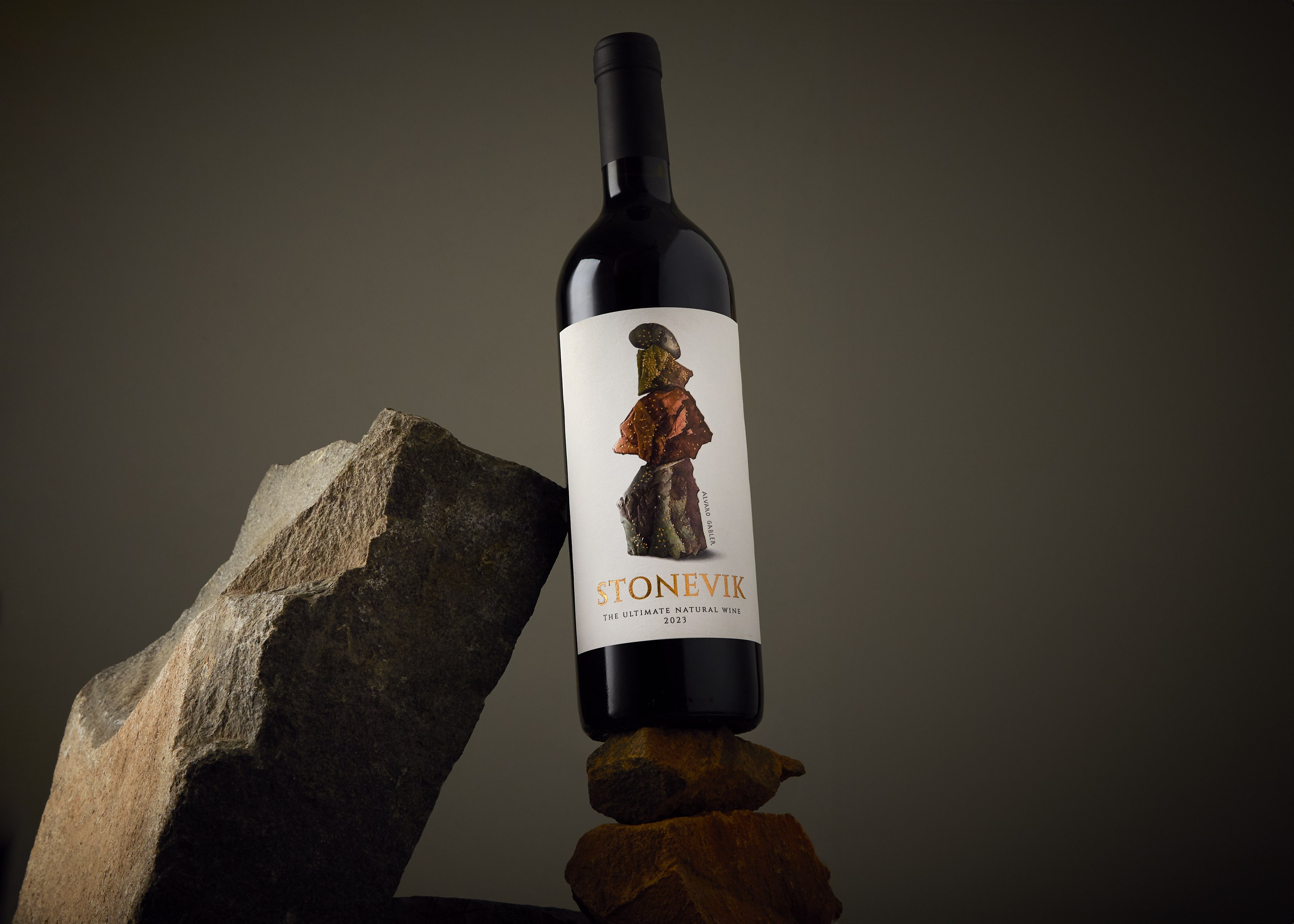 Botella de STONEVIK equilibrada sobre piedras minerales junto a un gran bloque de roca, con la obra de Álvaro Gabler visible en la etiqueta