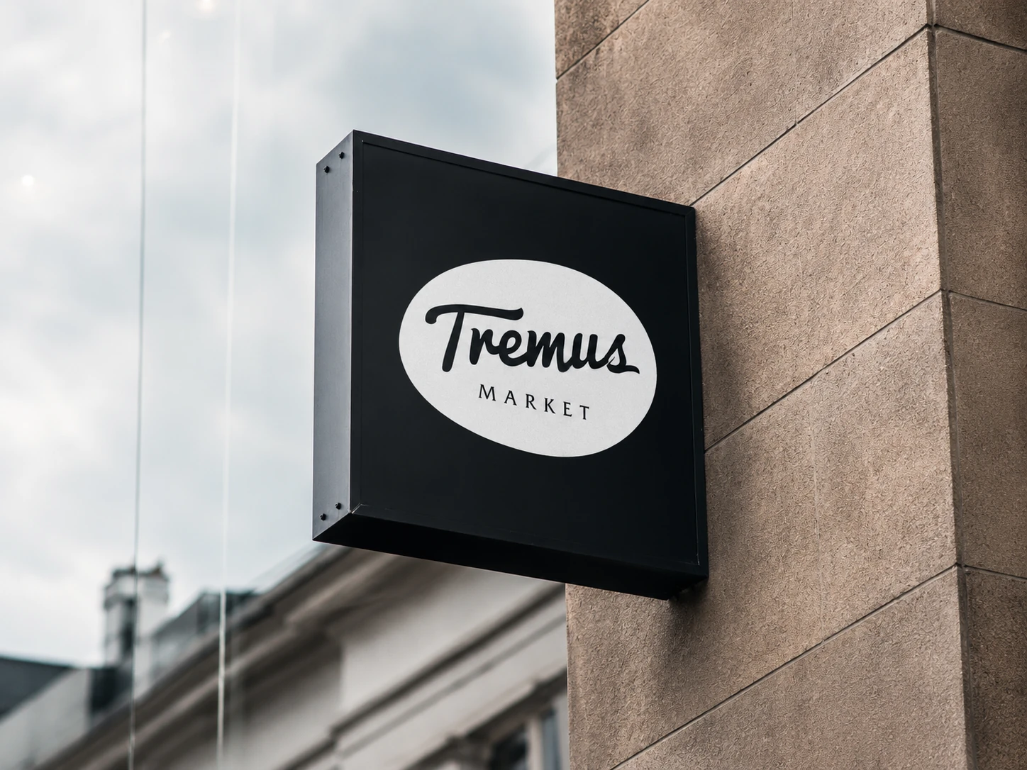 Tremus Market's facade sign in a black box with a white isologo, mounted on a stone wall.