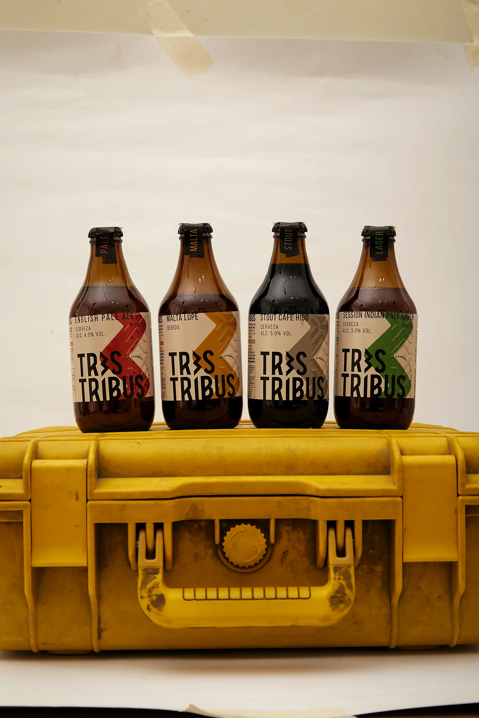 Las cuatro variedades de Tres Tribus alineadas sobre un estuche rígido amarillo: English Pale Ale, Malta Lupe, Stout Café Higo y Session Indian Pale Lager.