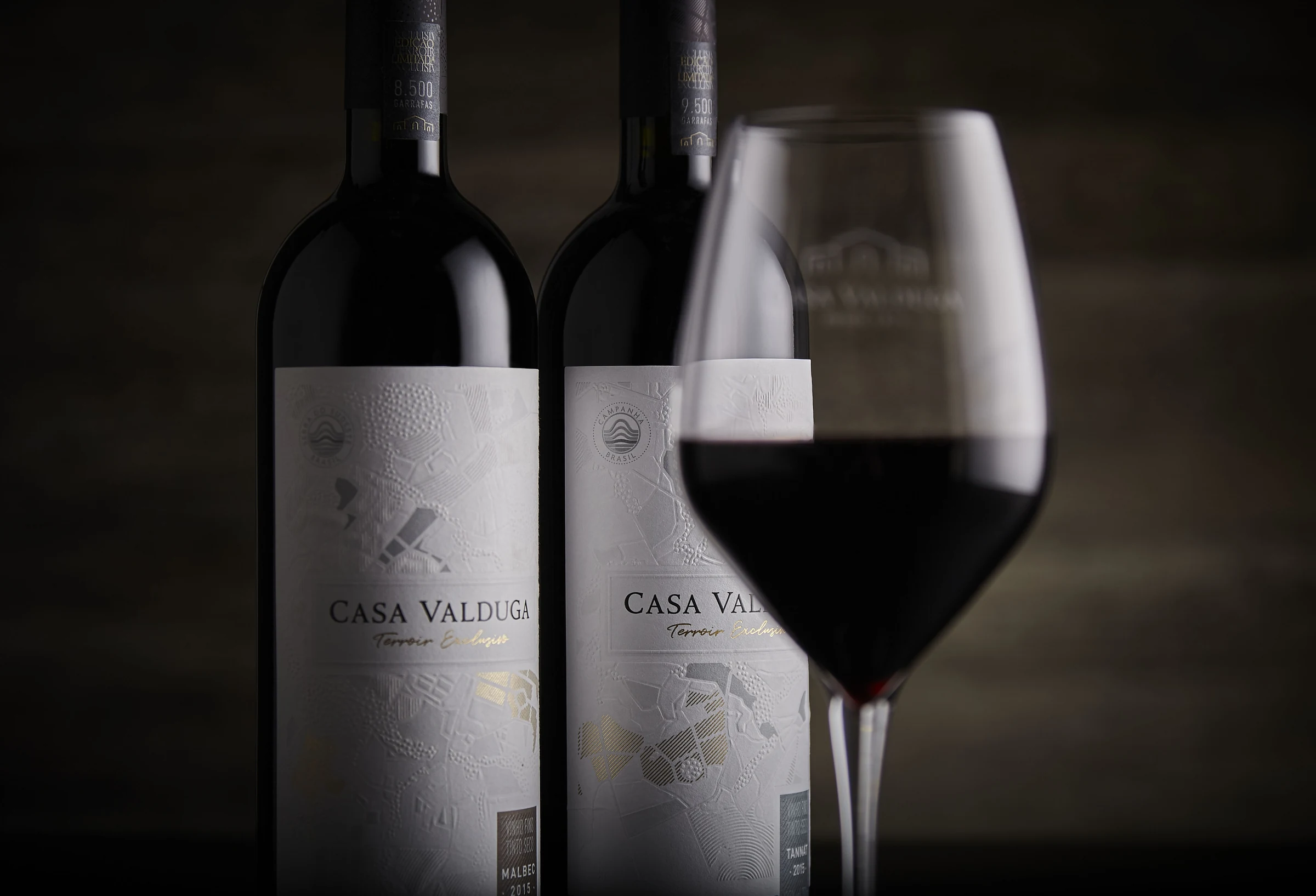 Dos botellas Casa Valduga Terroir junto a una copa de vino tinto.