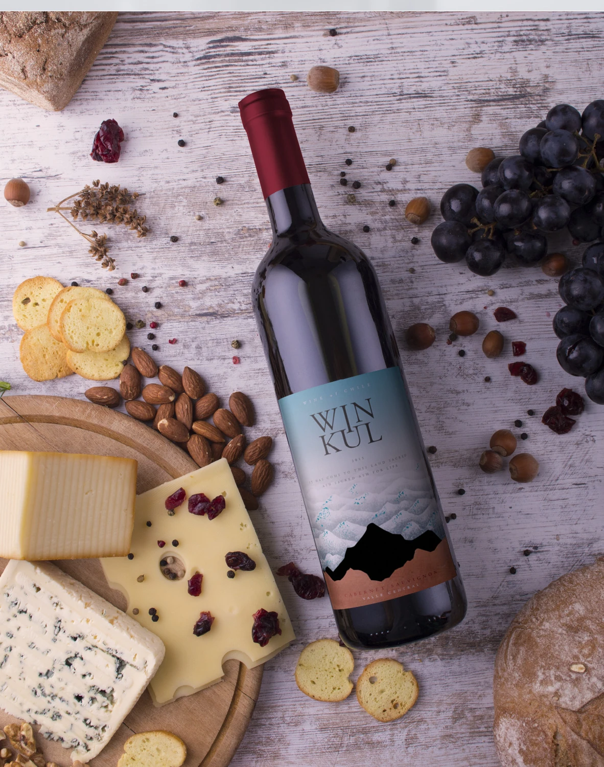 Botella Winkul sobre una mesa con quesos, frutos secos, uvas y pan.