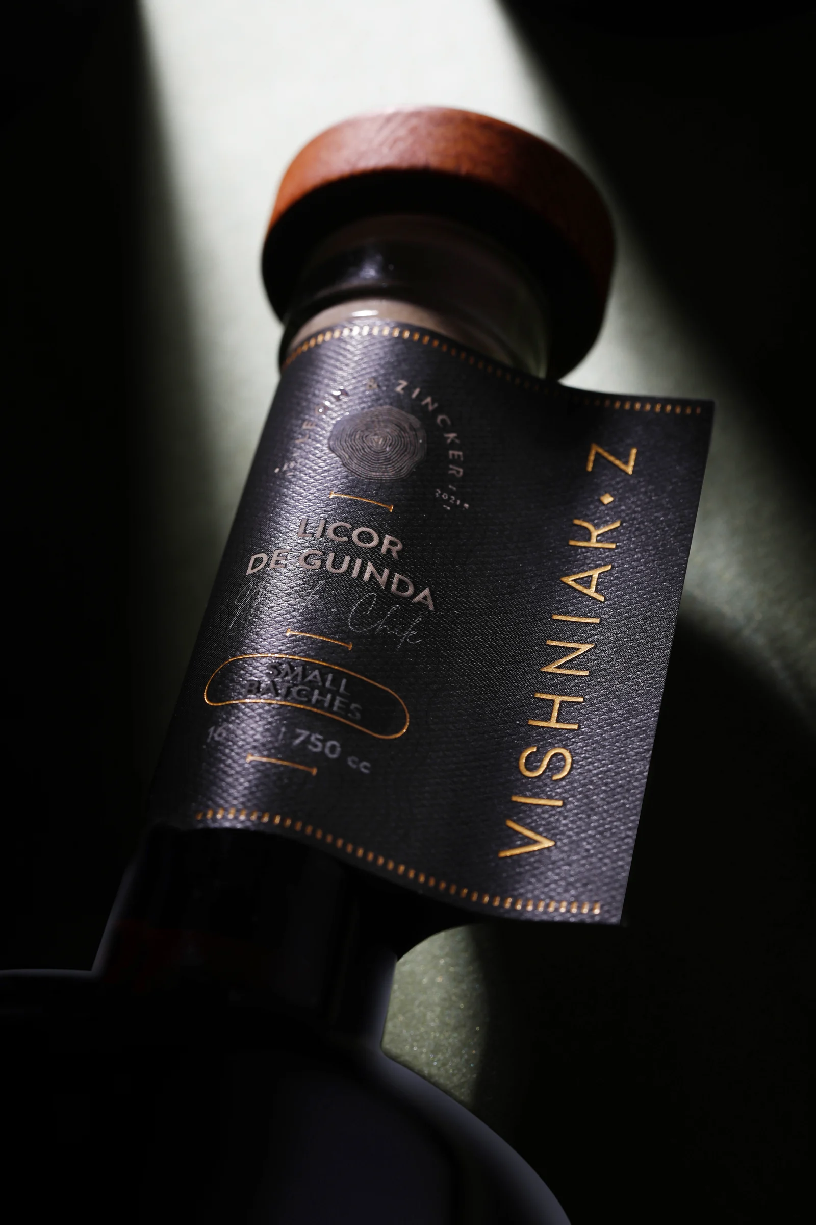 Detalle del cuello de la botella Vishniak Z: colgante negro con tipografía en cobre, sello de León & Zincker y tapón de madera.