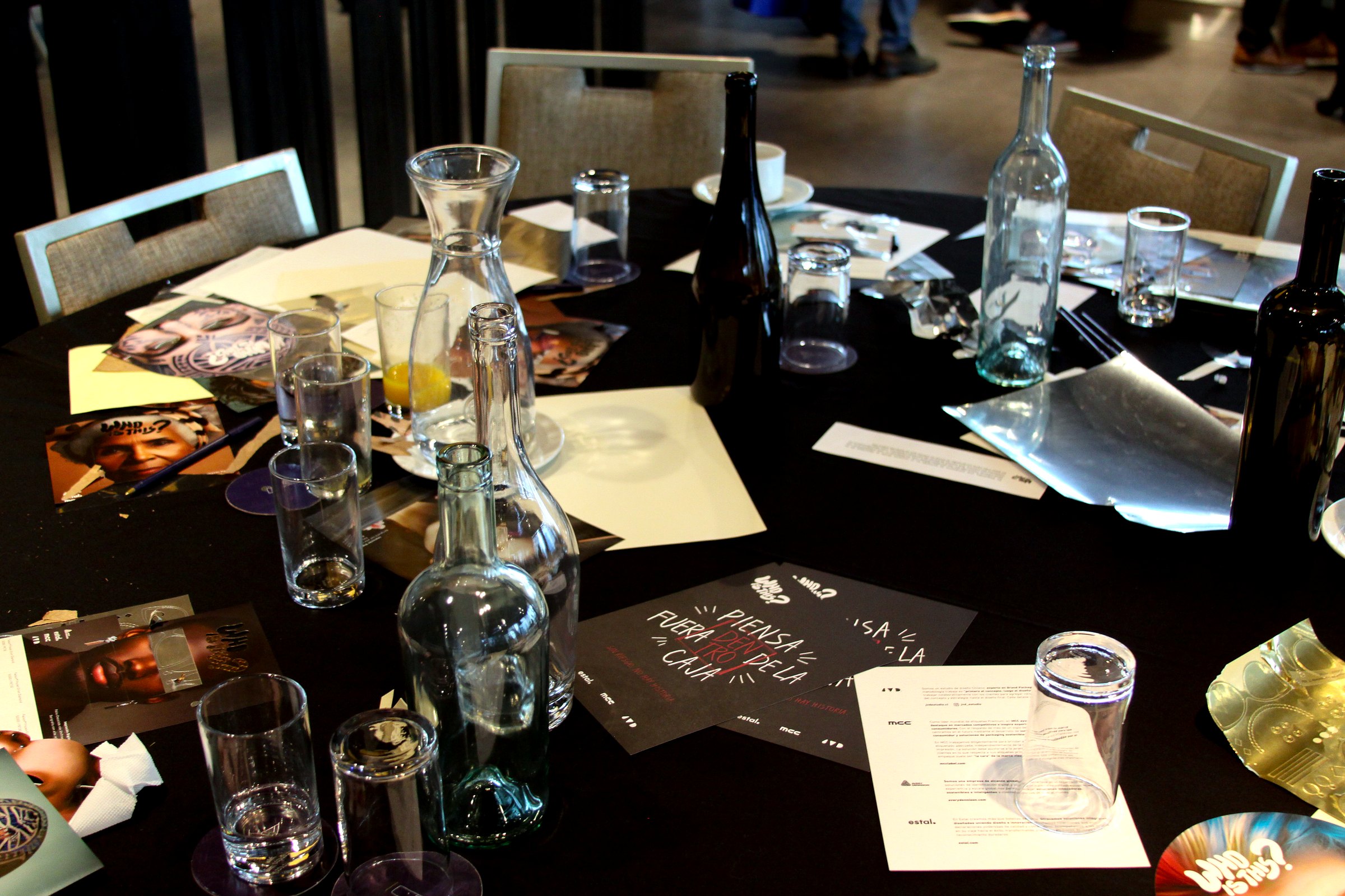 Mesa con botellas de vidrio, materiales y piezas gráficas durante el proceso de intervención del taller WHO IS THIS
