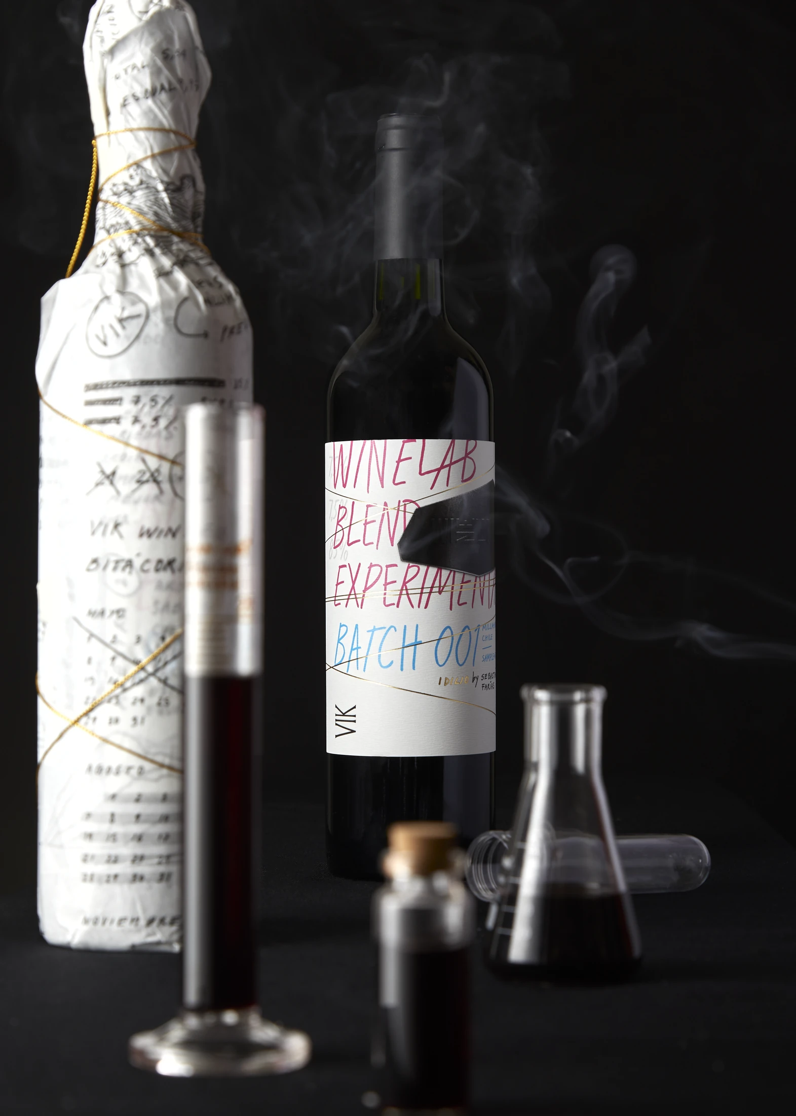 Bodegón de la edición 2023: botella envuelta en papel anotado, botella final y material de laboratorio sobre fondo oscuro.