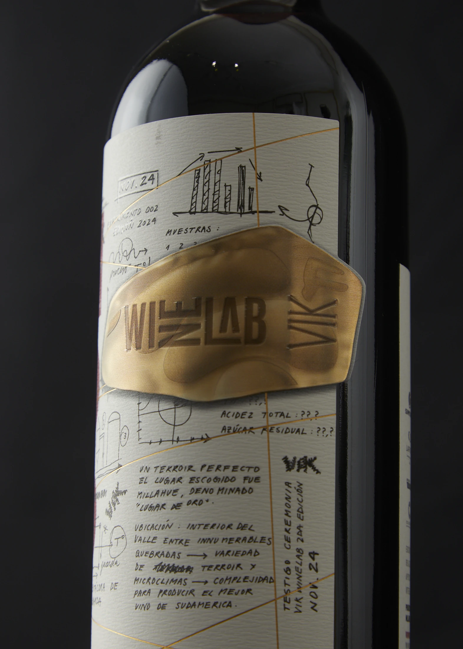 Detalle de la botella WineLab 2024: etiqueta con anotaciones a mano y un parche de foil dorado con el logotipo.