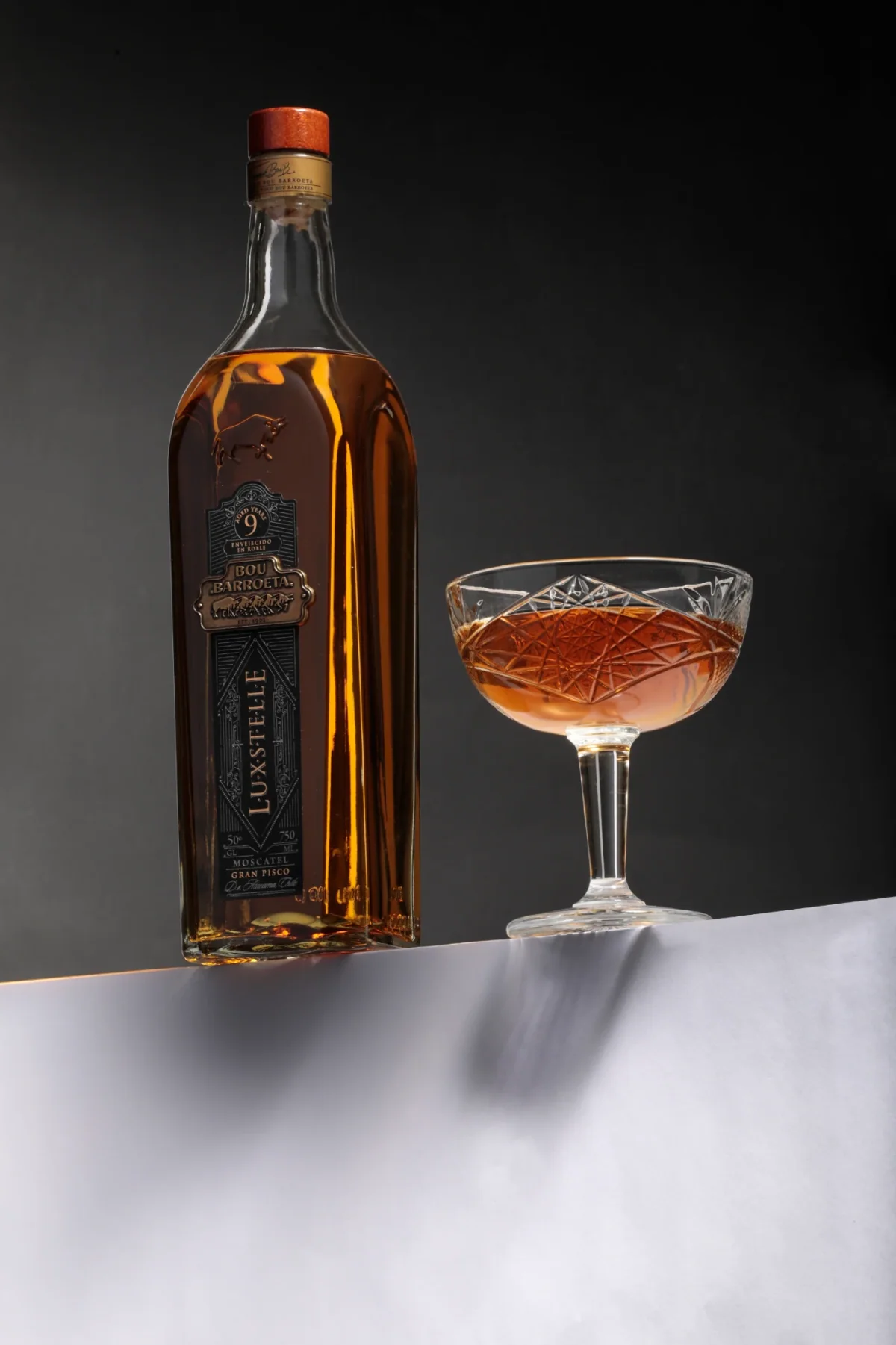 Botella Luxstelle de Bou Barroeta junto a una copa coupe servida, sobre fondo oscuro.