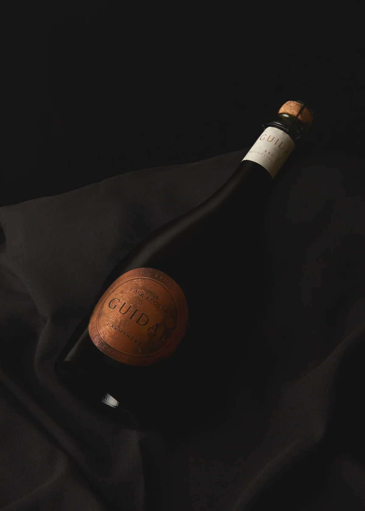 Botella Guidaí sobre seda negra, con el medallón de cobre en relieve como único punto de luz.