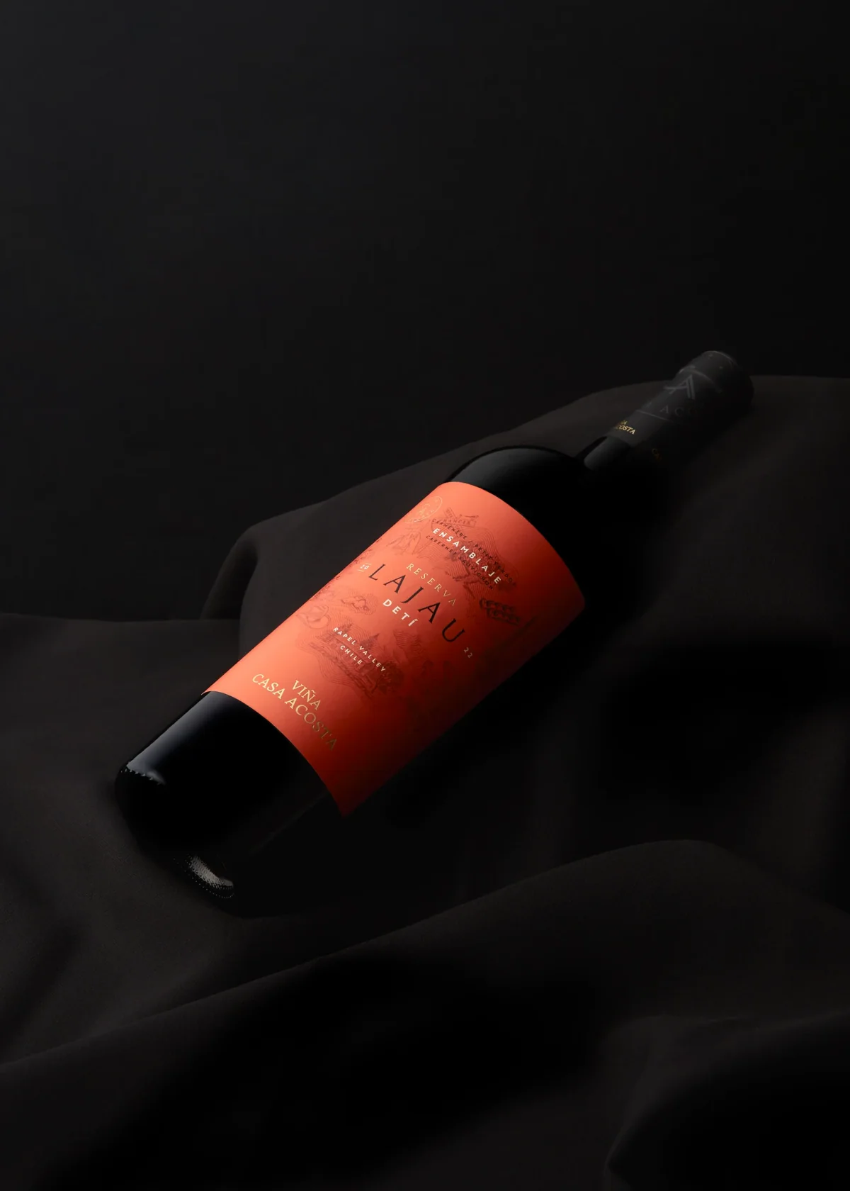 Botella Lajau DETÍ con la etiqueta naranja sobre seda negra, iluminada contra un fondo en penumbra.