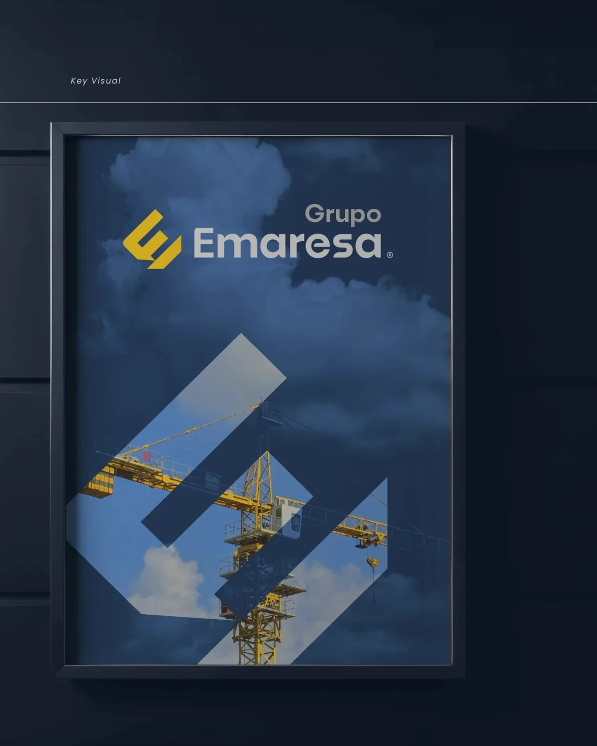 Key visual de Grupo Emaresa: isotipo E/M aplicado sobre una fotografía de grúa contra el cielo