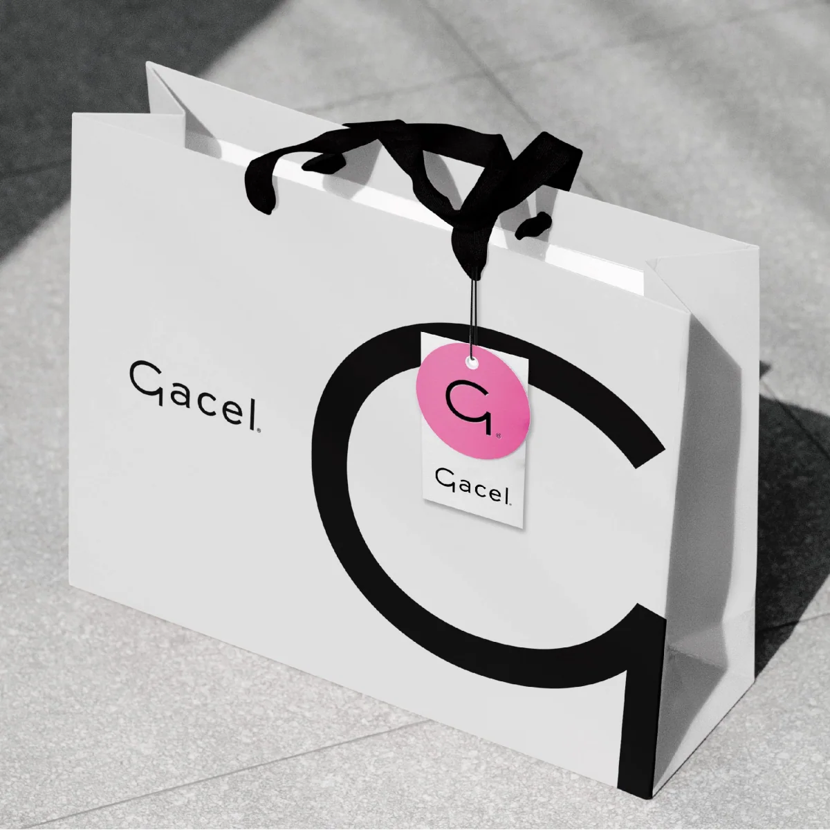 Bolsa de regalo Gacel en blanco y negro con isotipo G y colgante rosado.