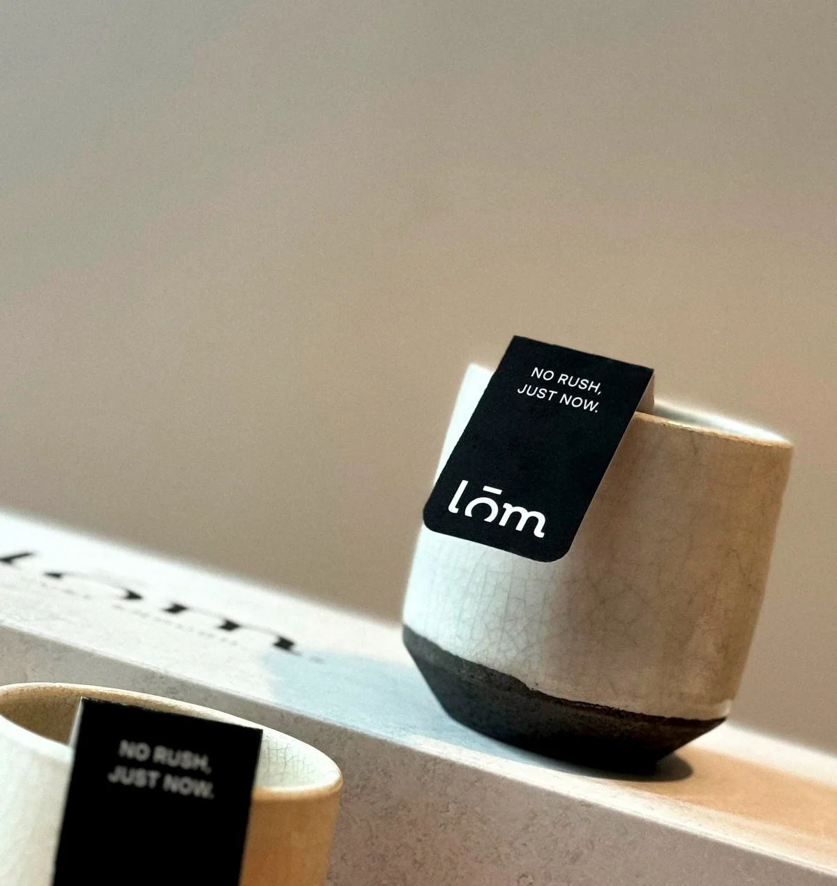 Tazas de cerámica con la etiqueta de anclaje LŌM «No rush. Just now.» sobre la caja de té.