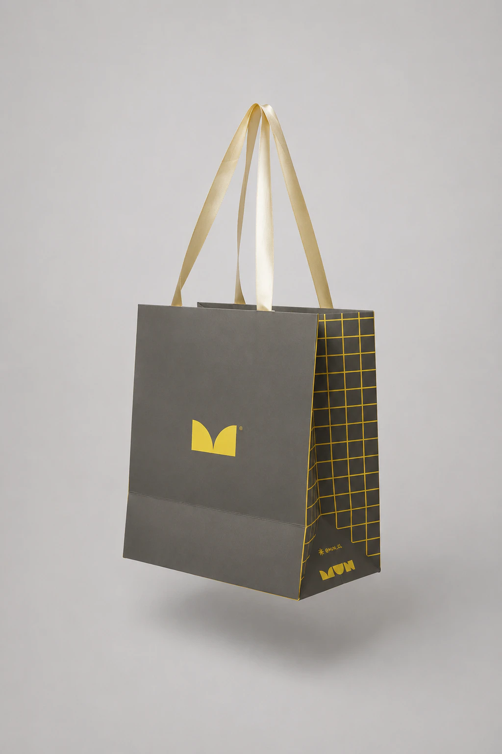 Bolsa MUN gris con asas claras, isotipo amarillo y retícula lateral.
