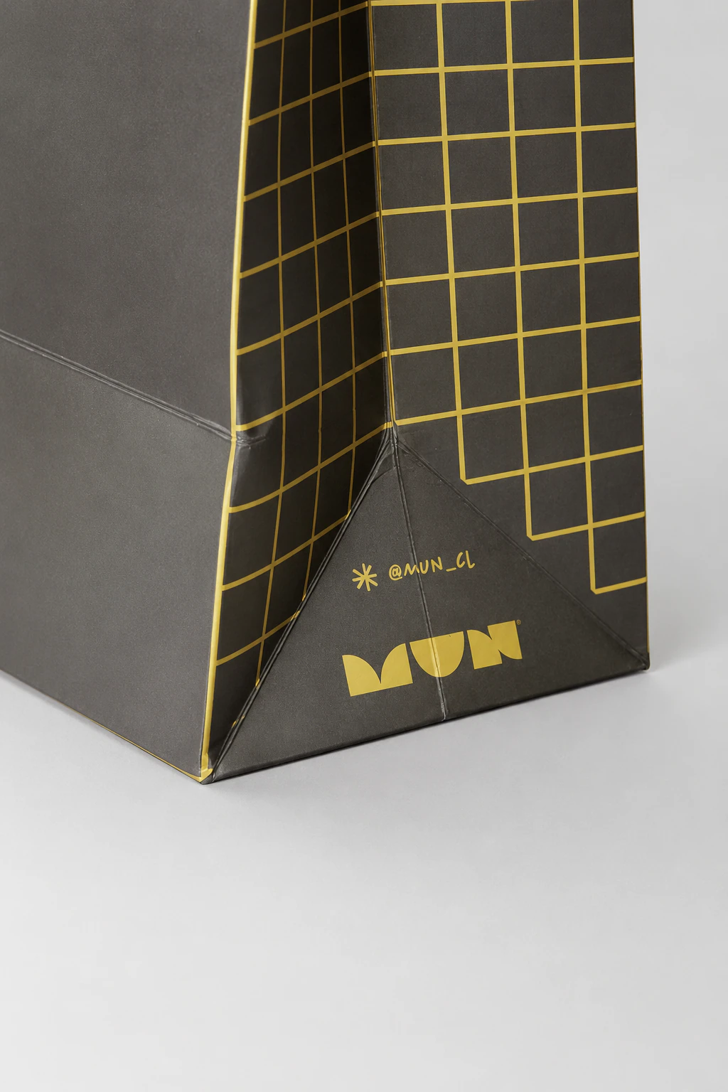 Detalle lateral de una bolsa MUN con retícula amarilla, logotipo y usuario @mun_cl.