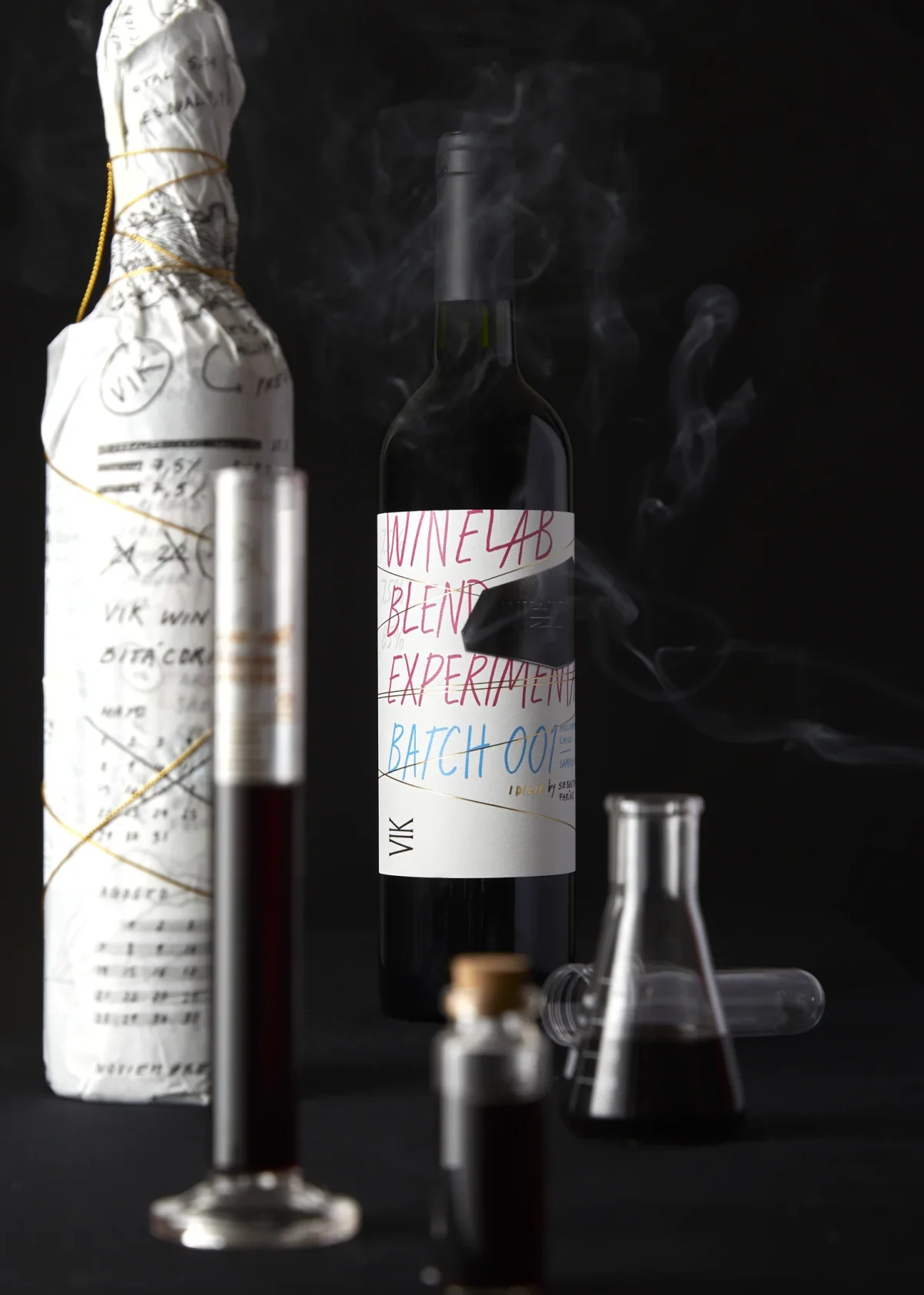 Bodegón de la edición 2023: botella envuelta en papel anotado, botella final y material de laboratorio sobre fondo oscuro.