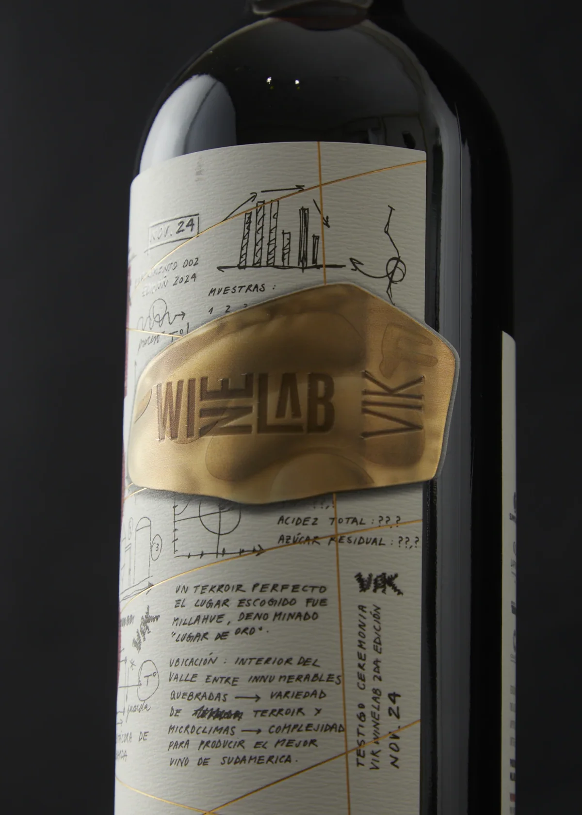 Detalle de la botella WineLab 2024: etiqueta con anotaciones a mano y un parche de foil dorado con el logotipo.