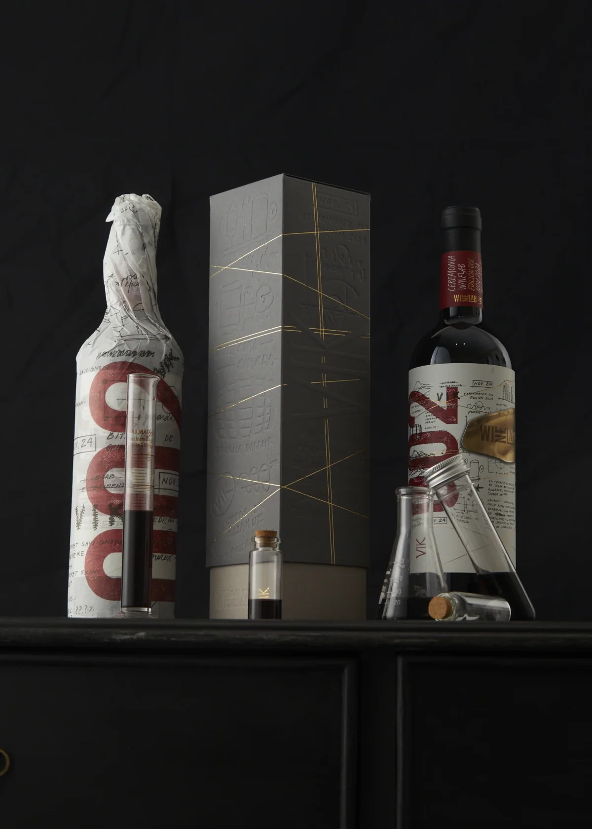 Edición 2024 de VIK WineLab: la botella envuelta en papel anotado con el numeral 002, el estuche gris con relieve y líneas de foil, y la botella final con su etiqueta escrita a mano.