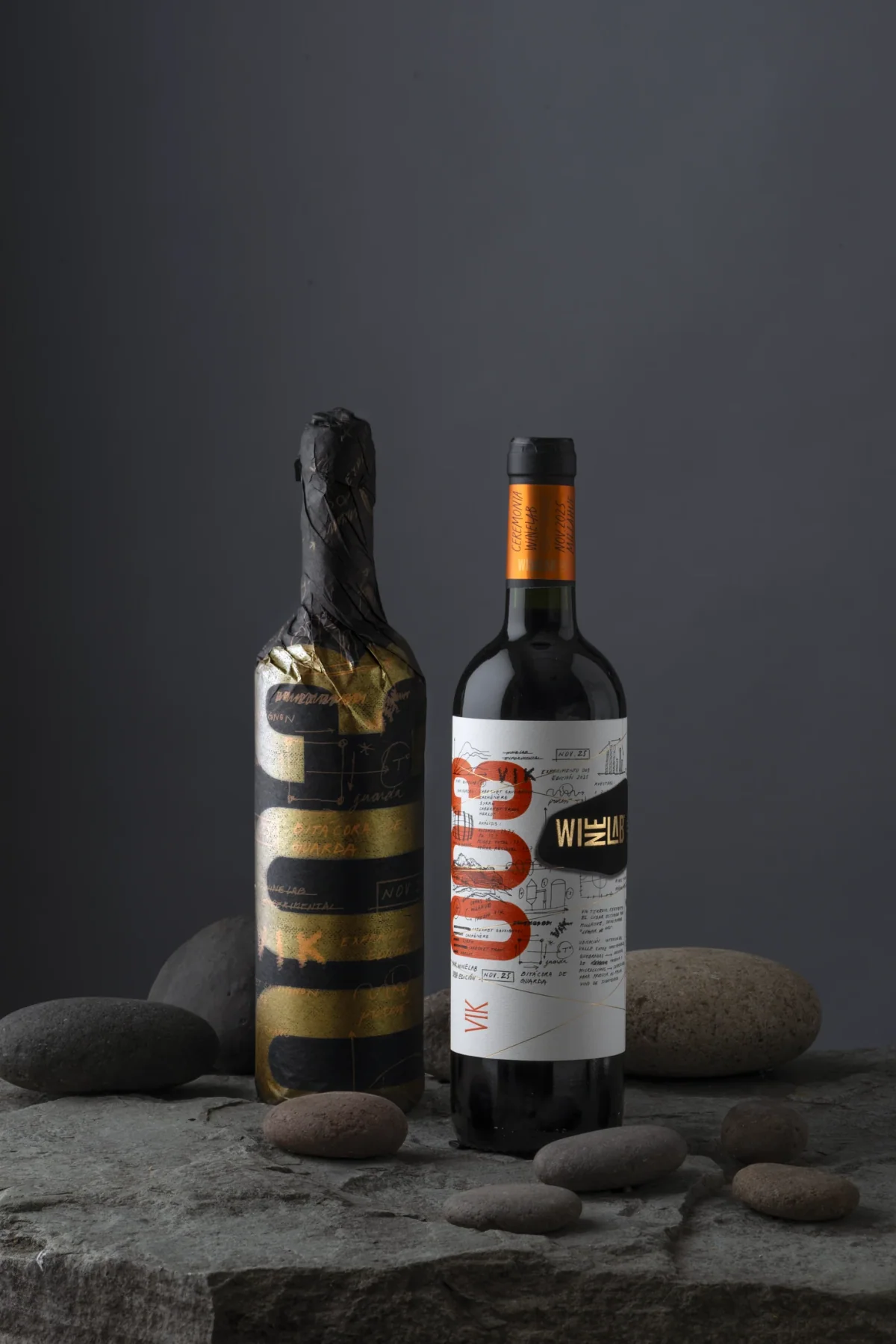 Edición 2025 de WineLab: la botella envuelta en papel negro y oro junto a la botella final de etiqueta clara con el numeral 003 en naranjo, sobre piedras.